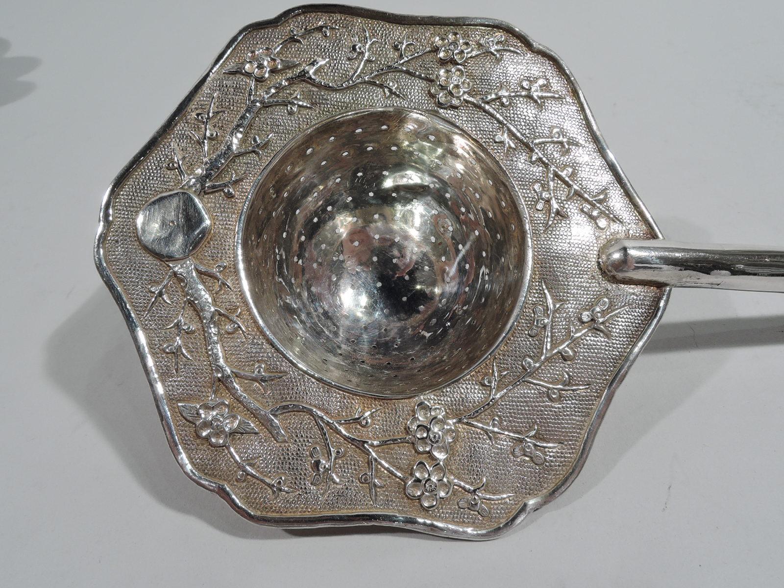 Chinese silver tea strainer, ca 1910. Deep and pierced bowl and wide shoulder with blossoming prunus branch on stippled ground; rim scrolled. Plain cylindrical handle. Cylindrical handle. Unmarked. Weight: 2 troy ounces.