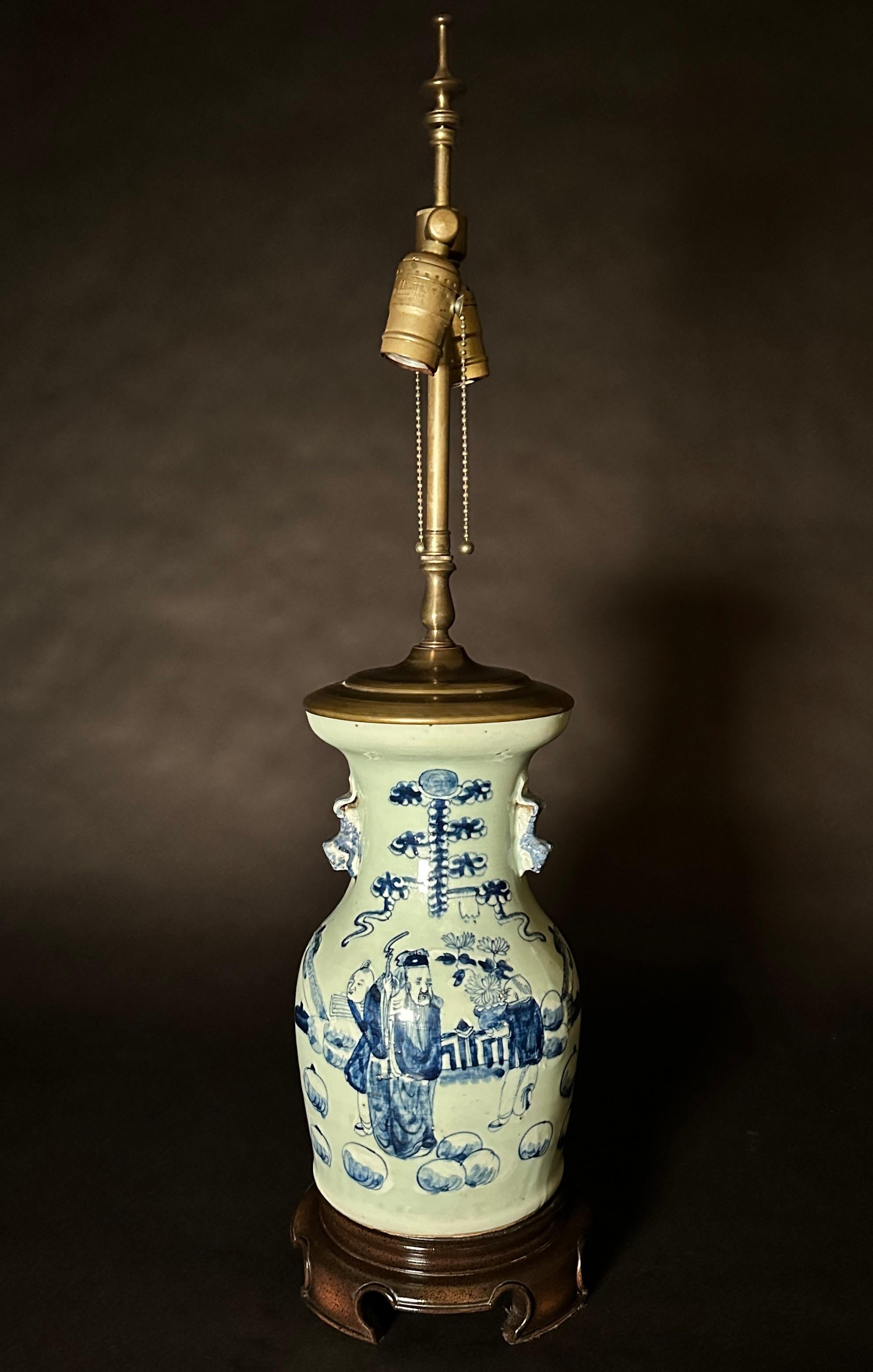 Vase chinois du 19e siècle en porcelaine bleue et blanche transformé en lampe. Peint à la main avec des personnages chinois dans une cour, sur un fond céladon clair et décoré de motifs appliqués.  poignées de foo dog. Monté sur une base en teck