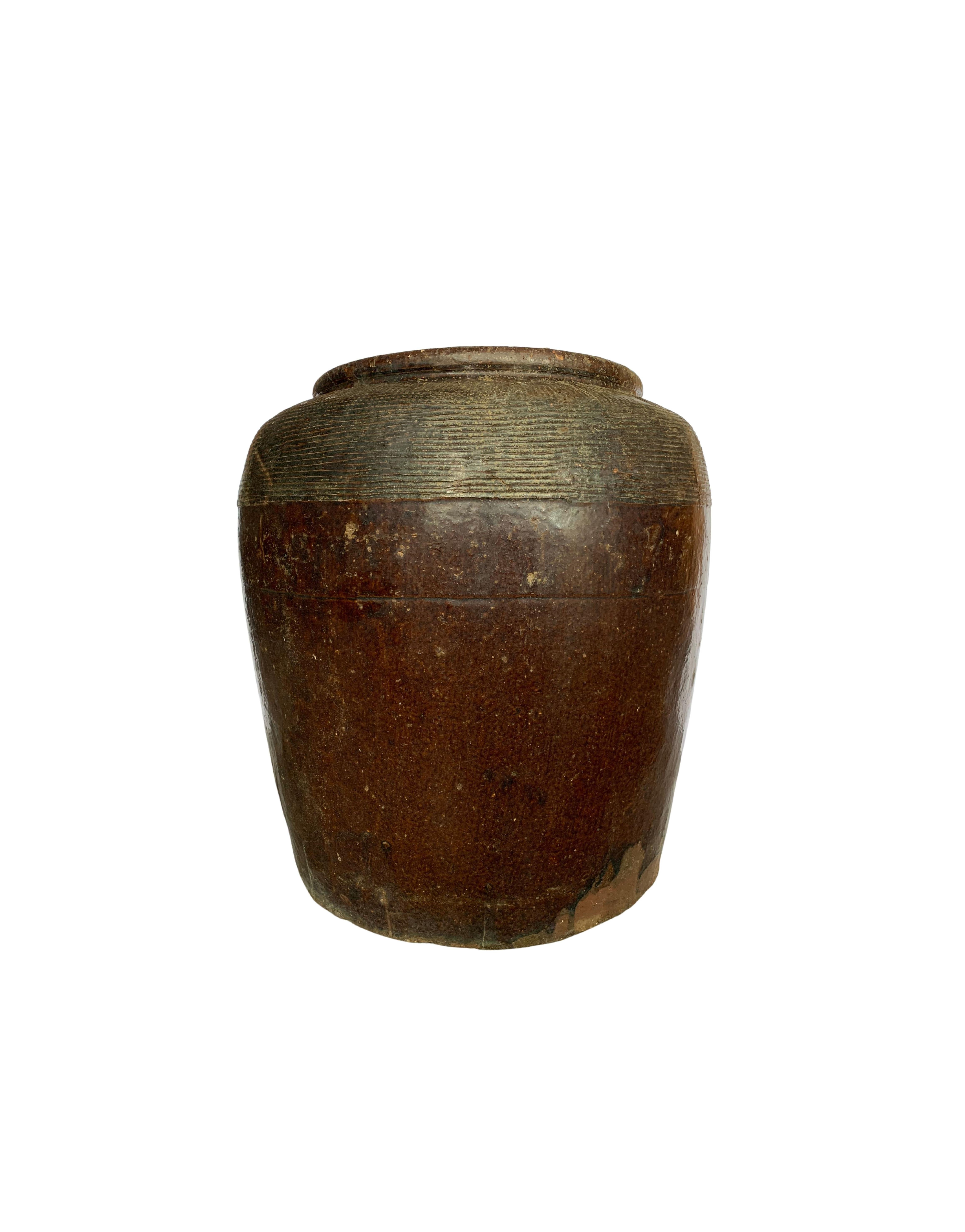 This Antique Jar dating to the early 1900s once served the purpose of crafting salty eggs. The jar features a wonderful brown glaze. There is a ridged pattern finish near to the Jar's rim. The jar is visibly old with the fading and markings to the