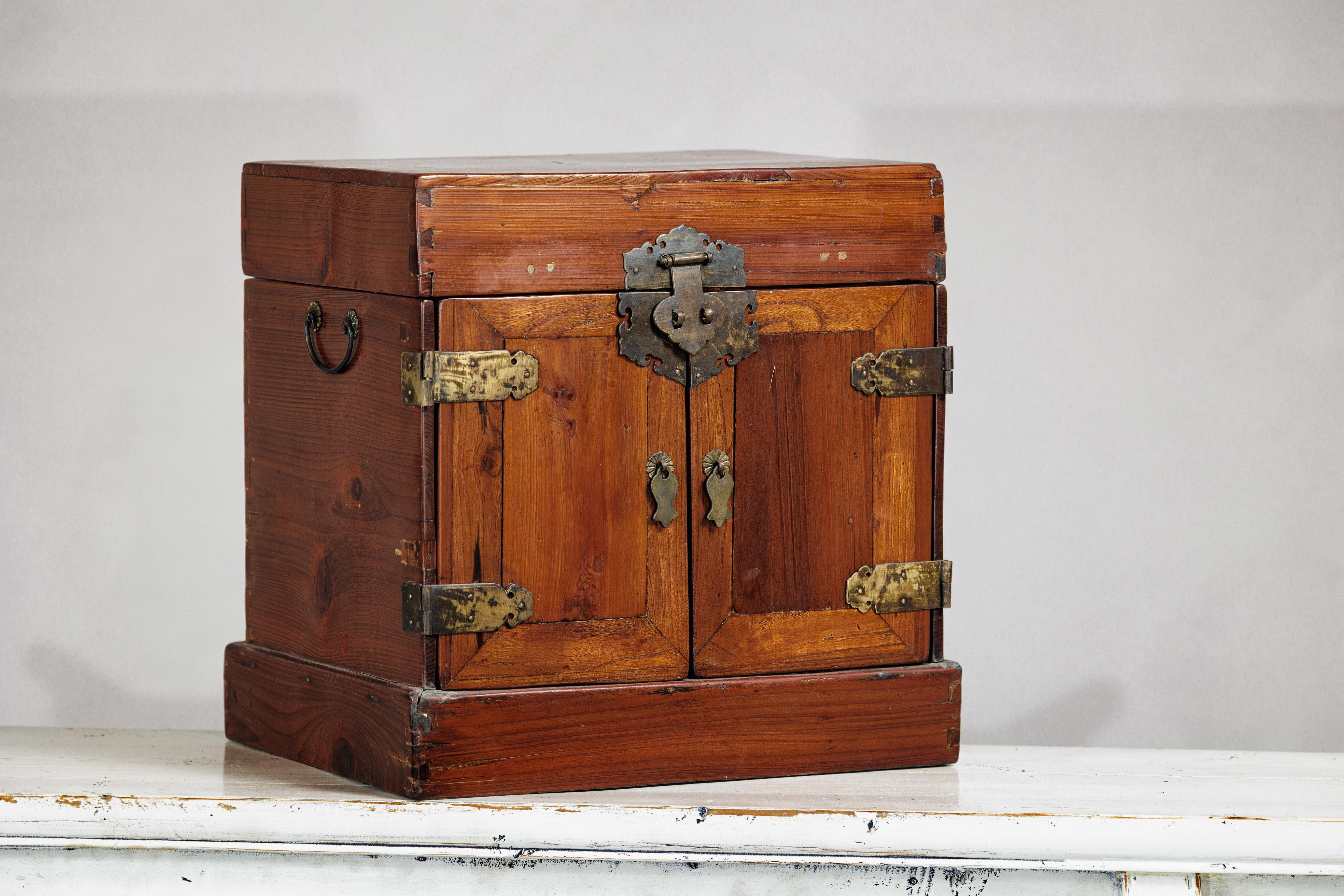 Este antiguo tocador chino presenta un cálido acabado lacado marrón sobre madera blanda, con un rico veteado y una forma compacta y rectangular. Probablemente de principios del siglo XX, el maletín se abre por la parte superior para revelar un