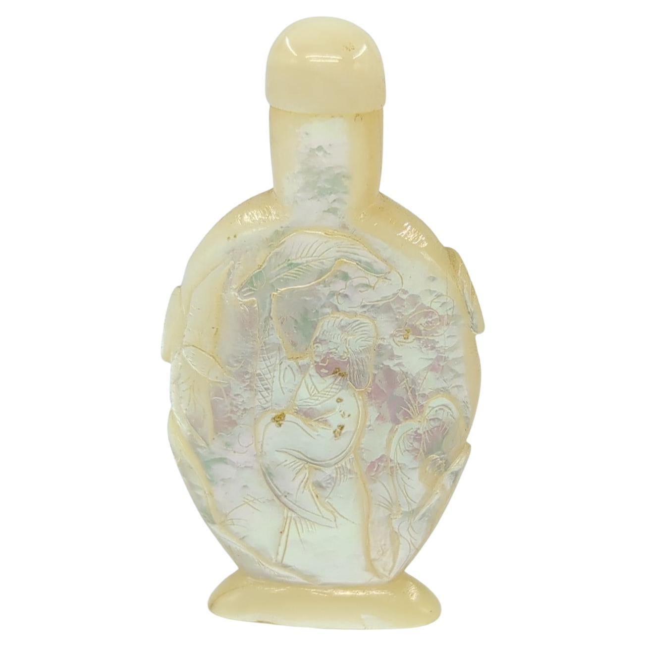 This vintage Chinese snuff bottle, exquisitely crafted from mother of pearl (MOP), is a fine example of cameo carving, a technique that creates raised relief images by carving into the layers of the material. The bottle features incised details that