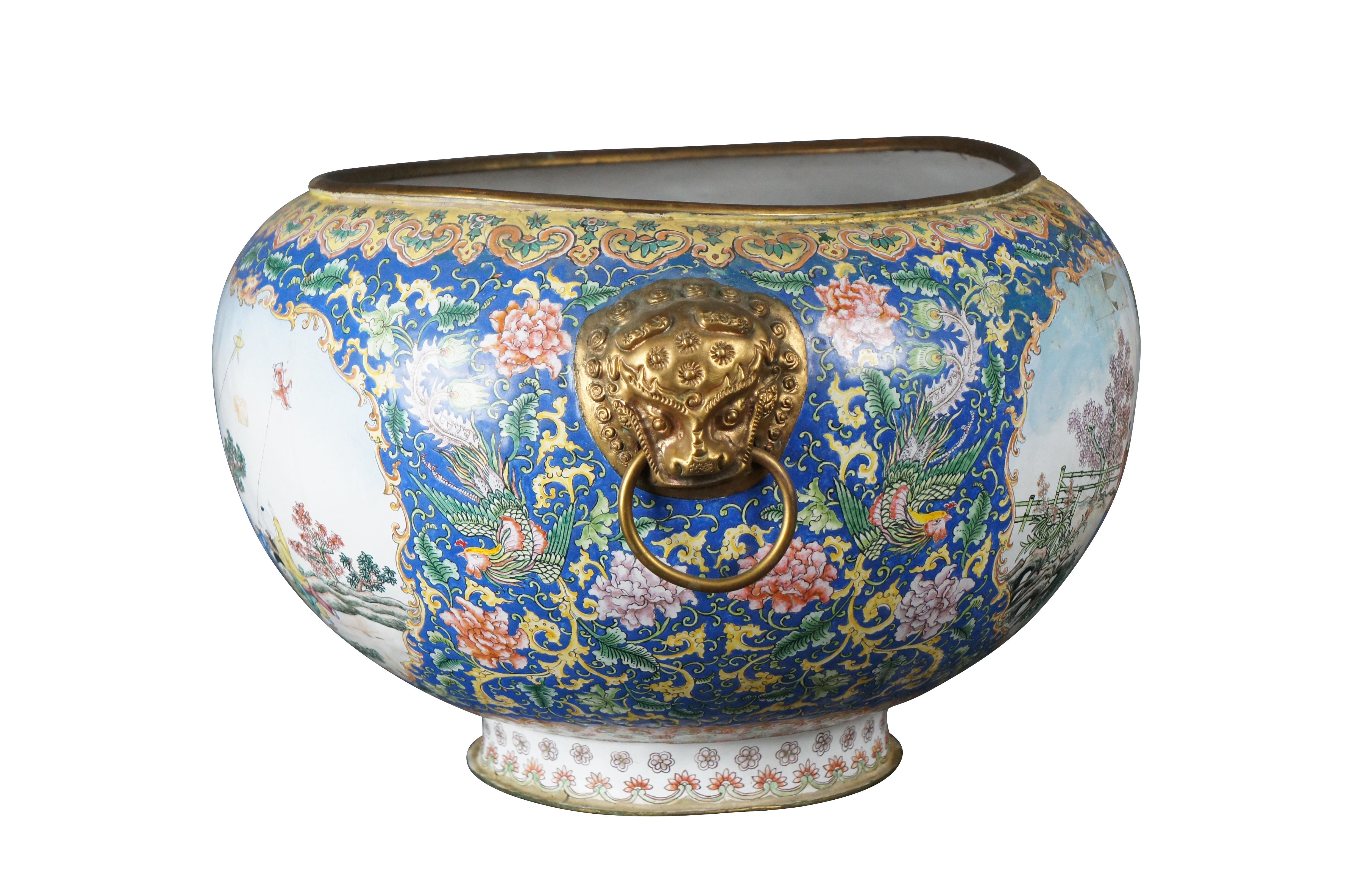 A large Chinese Canton Enamel Jardinière, circa 1900s. Features an ovoid form between two gilded metal animal masks with hoop handles. The bowl is decorated in bright enamels with a large cartouche showing a Chinese family flying animal figured