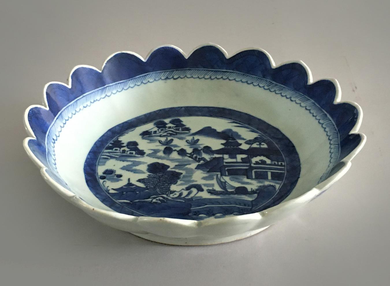 Chinese export Canton porcelain deep blue and white scalloped bowl. The inside is decorated with the traditional scene of pagodas, water, boats, rockery and trees. The outside surface is decorated with three sprigged flowers.