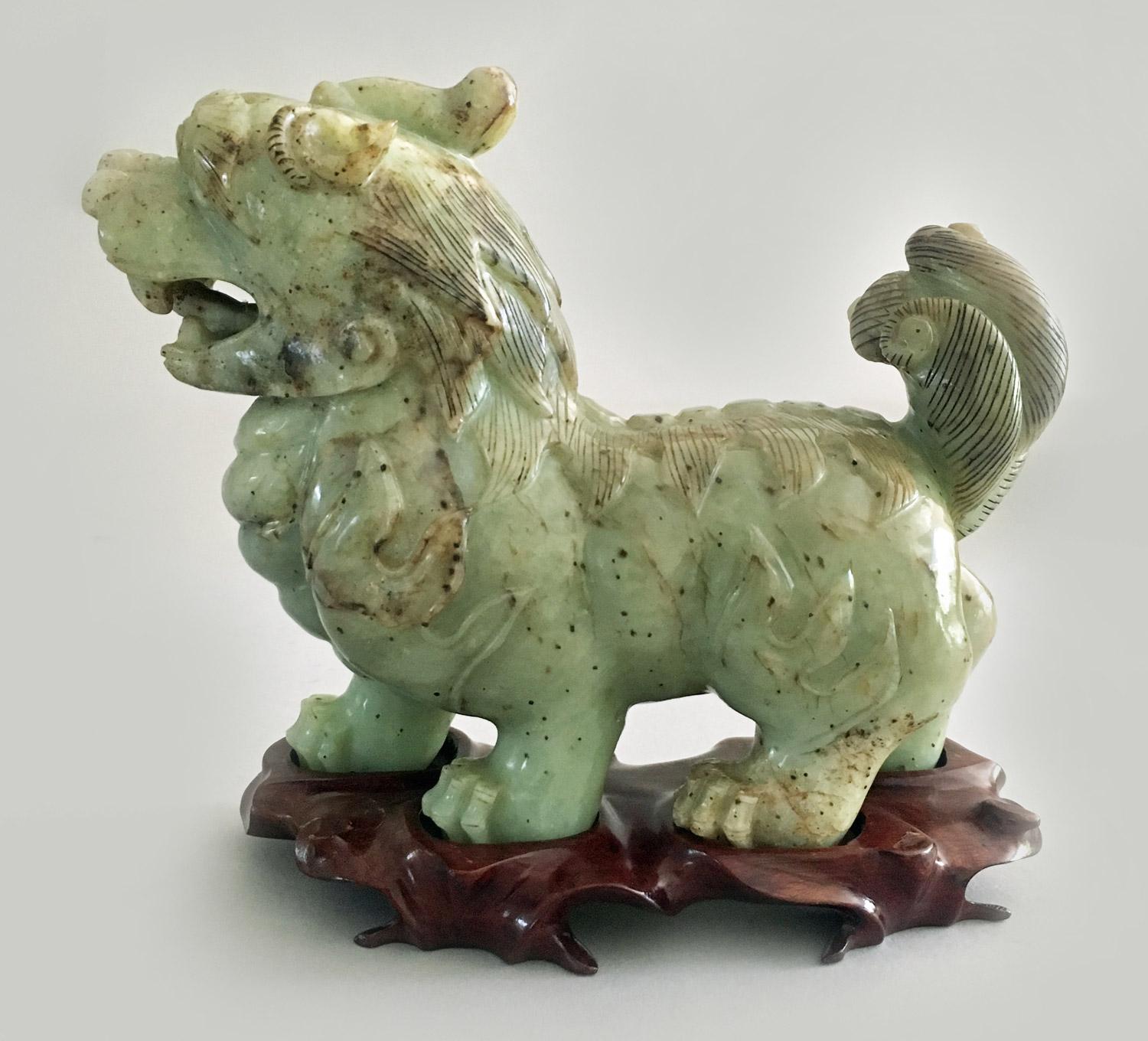 Chinese carved jade standing buddhistic lion with growling features and raised tail on a carved hardware stand.