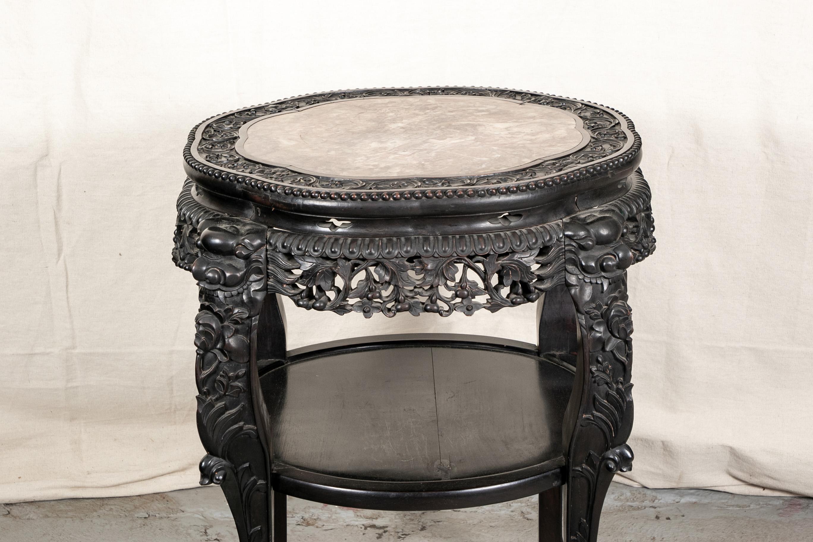 Dark stained and elaborately carved wood with a lower tier with lip. The shaped round top with a scrolled floral band with inset variegated marble top. The carved openwork frieze with four heavy carved legs with bird masks and floral motifs. Shaped
