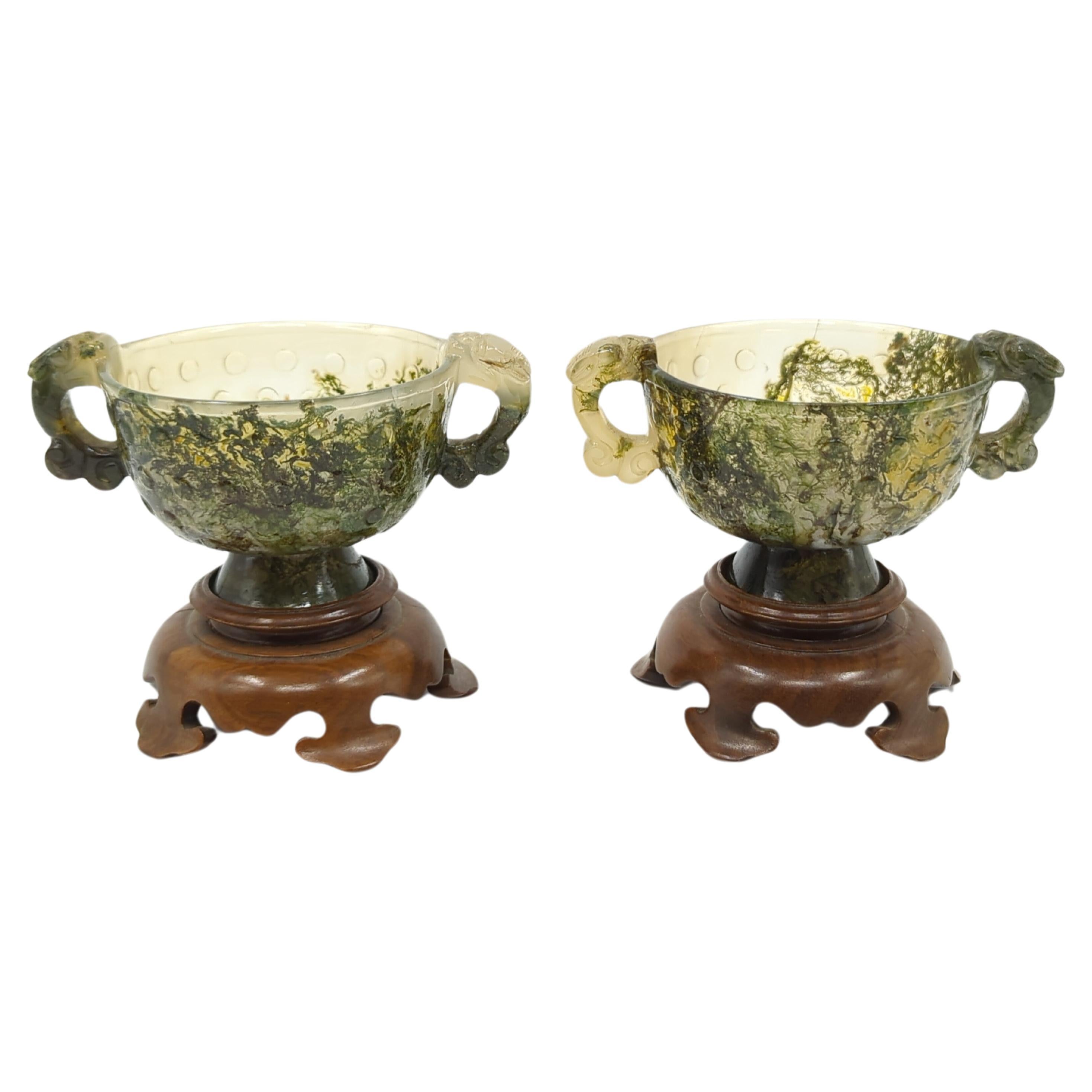 A fine garniture pair of Chinese moss agate carved cups, sides flanked with Qilin handles, relief carved raised grain patterns to exterior of body, thinly lipped mouth ring, and on outward flaring high foot ring. 

Comes with finely carved ruyi