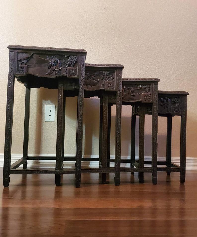 A set of four Chinese hardwood nesting tables from the early 20th century. Extensively hand carved with figural reliefs depicting Oriental folklore, each table graduated in size, fitting into the next, having rectangular top above carved legs,