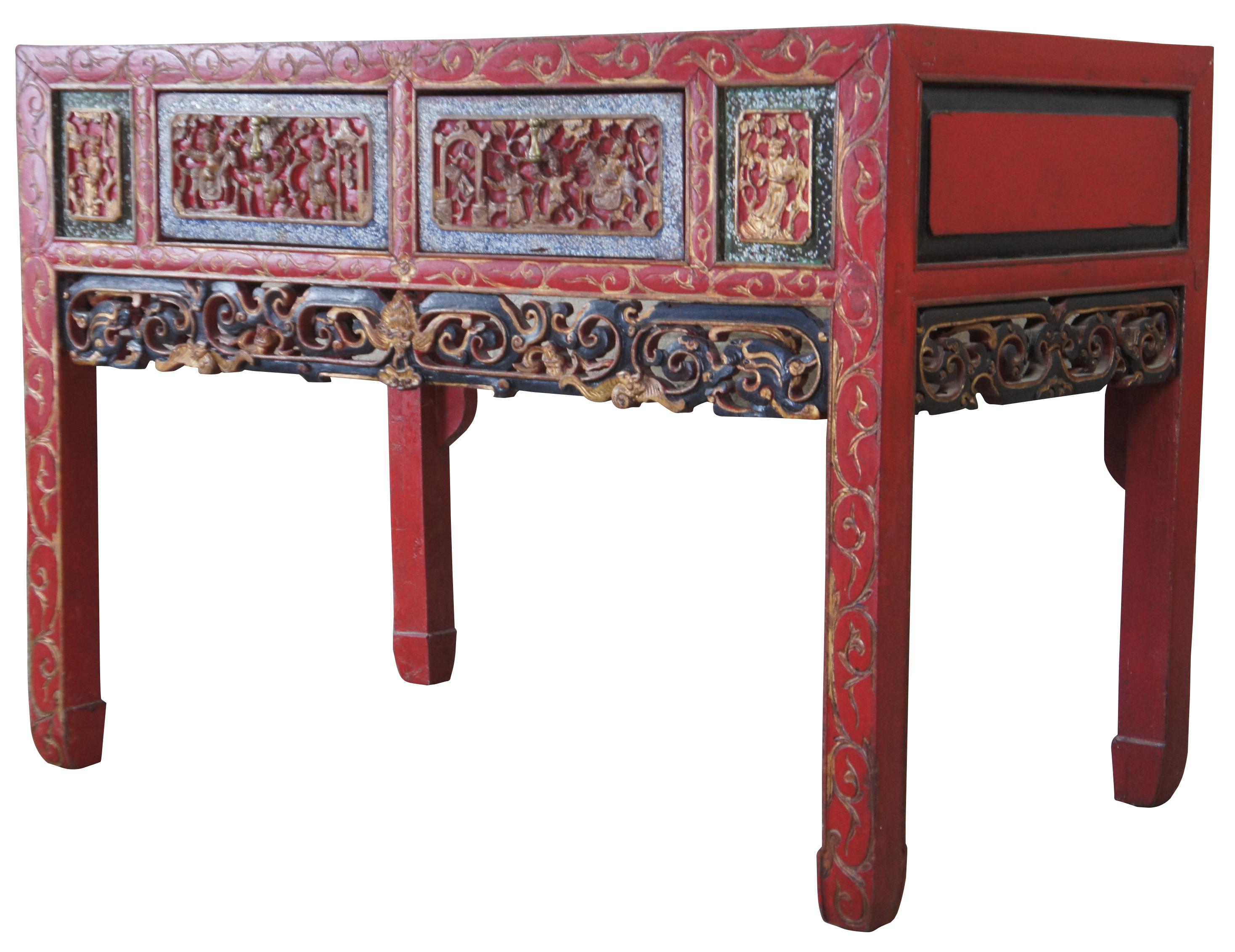 Antique Chinese altar table, circa 1900s. Features red painted exterior with carved high relief figures and a central bat below two dovetailed drawers. Measures: 42