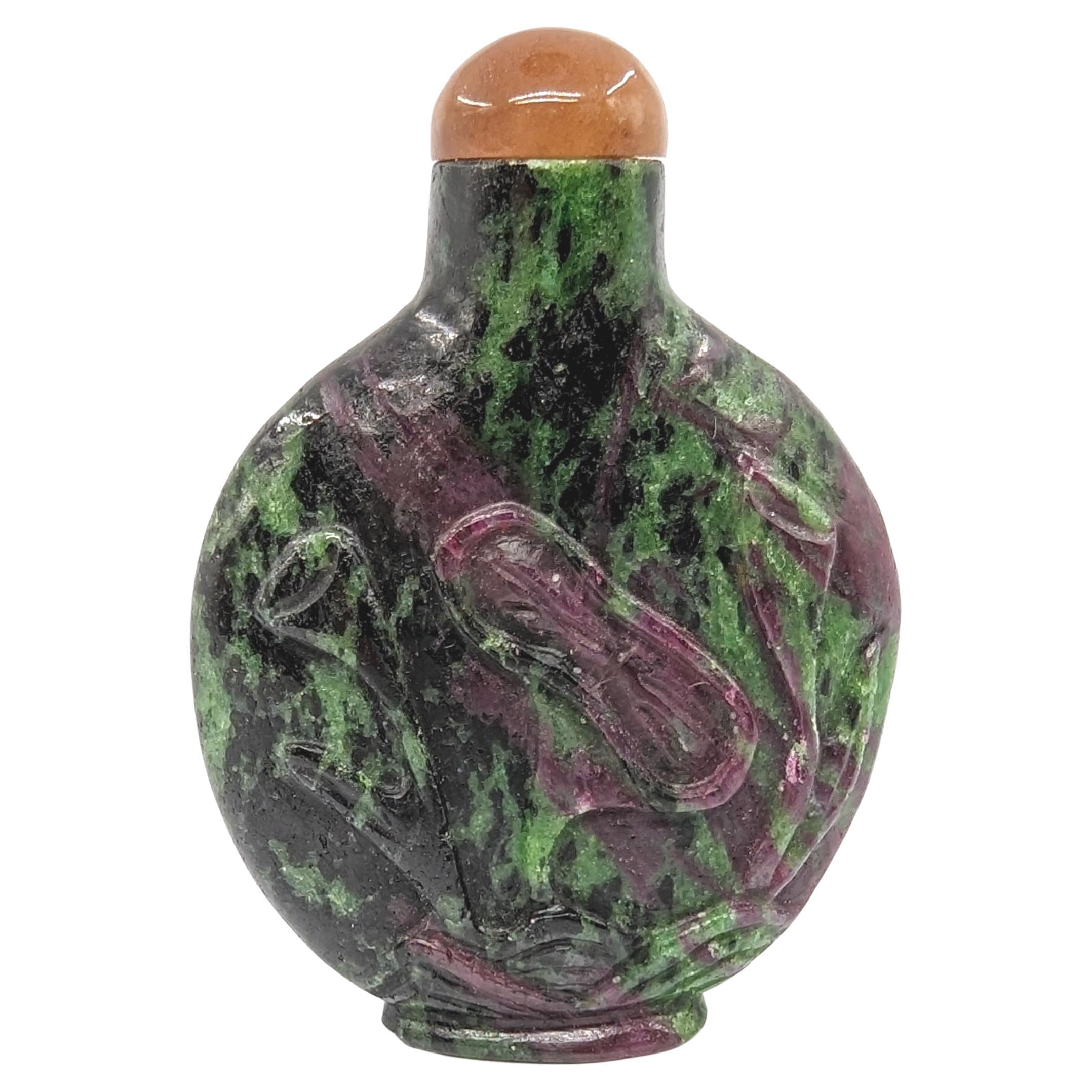 Antique Chinese carved ruby in zoisite hardstone snuff bottle, with carved lotus in relief accentuating the purple ruby in the material, raised on carved foot-ring, with a rounded agate stopper and red bone spoon

Early 20th century Republic period