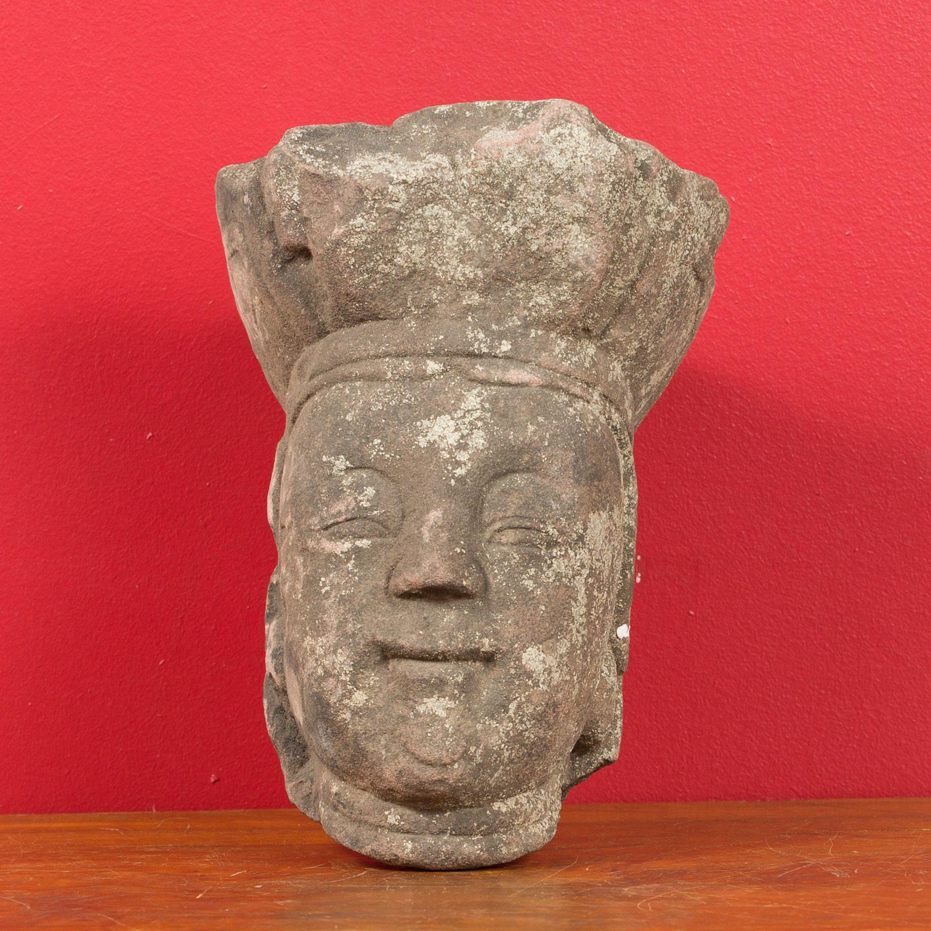 An antique Chinese carved stone head sculpture depicting a religious figure with nicely weathered appearance. Created in China, this carved stone sculpture will make for an excellent decorative object. Propped against a wall, the sculpture, likely