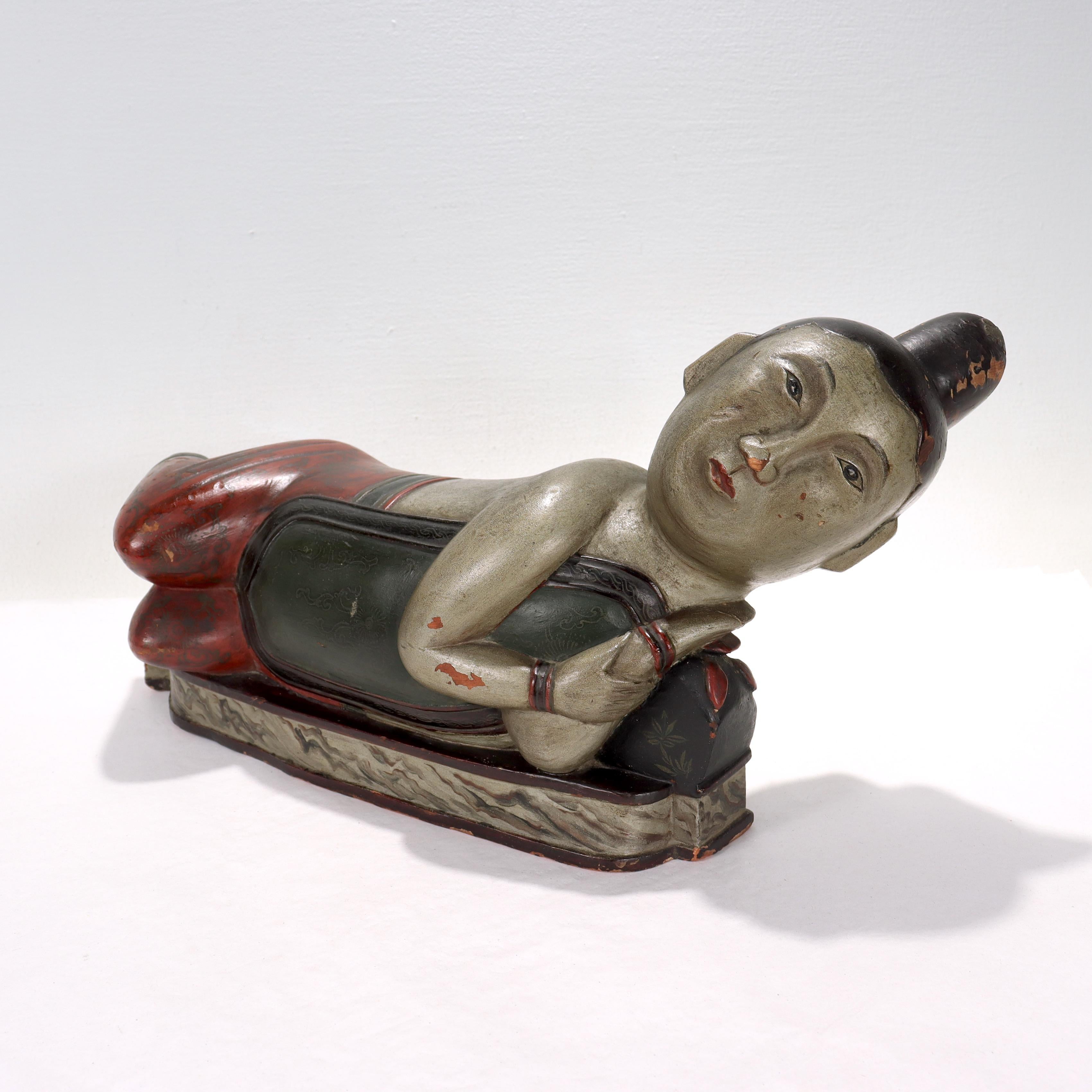 A fine antique Chinese wooden head rest.

Carved in the form of a recumbent or resting man.

Decorated in polychrome decoration. The body painted in a silver tone with his hair and eyes in black with red undertones. There is further scroll work