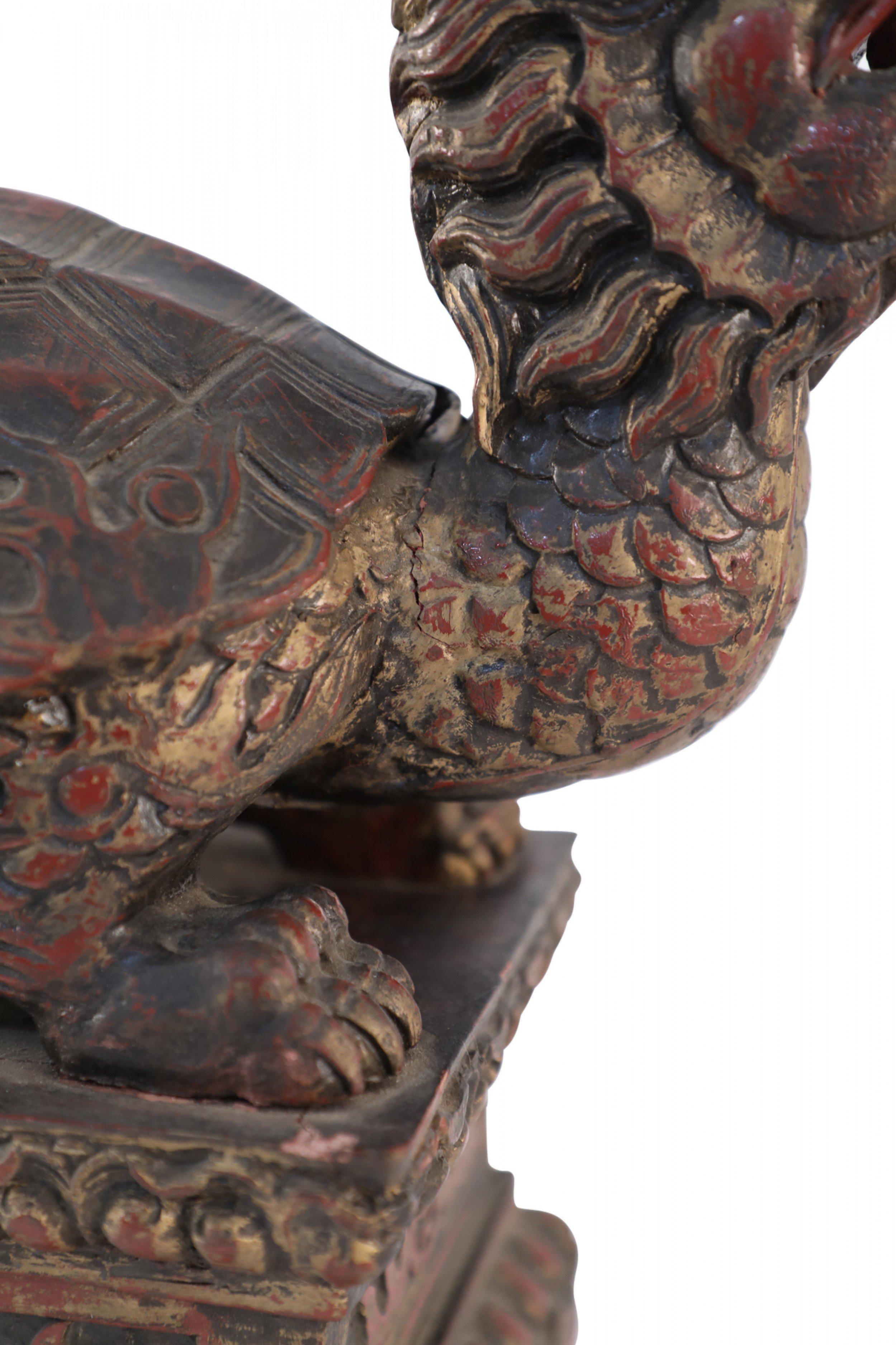 Antique Chinese carved wooden sculpture of a Longgui or (dragon turtle) holding a coin in its mouth on an ornately carved wooden base.
      