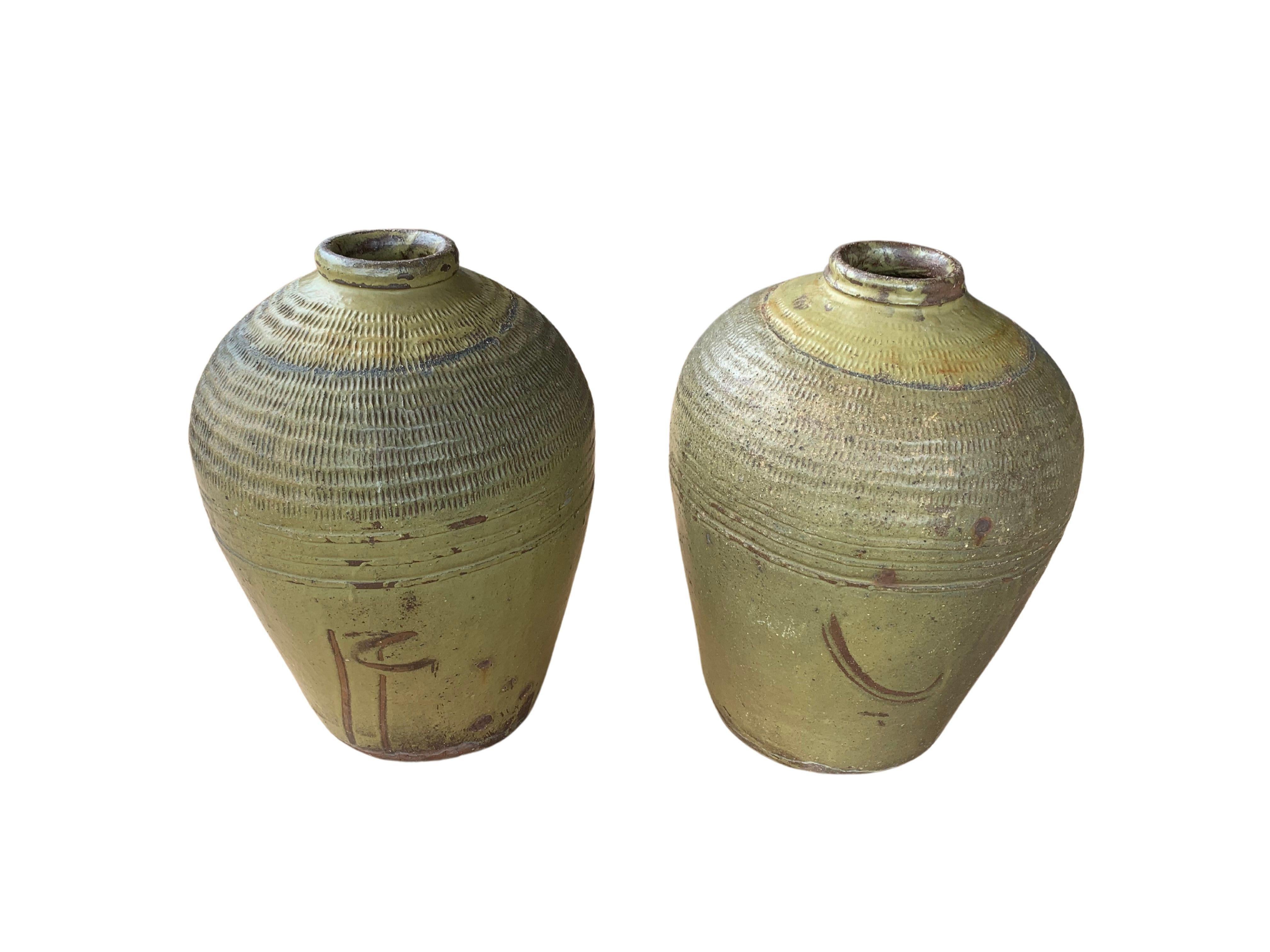 These glazed Chinese ceramic jars from the turn of the 19th century were once used for pickling foods. They feature a jade green finish and outer surface that features a ribbed texture. A great example of Chinese pottery, their imperfections and