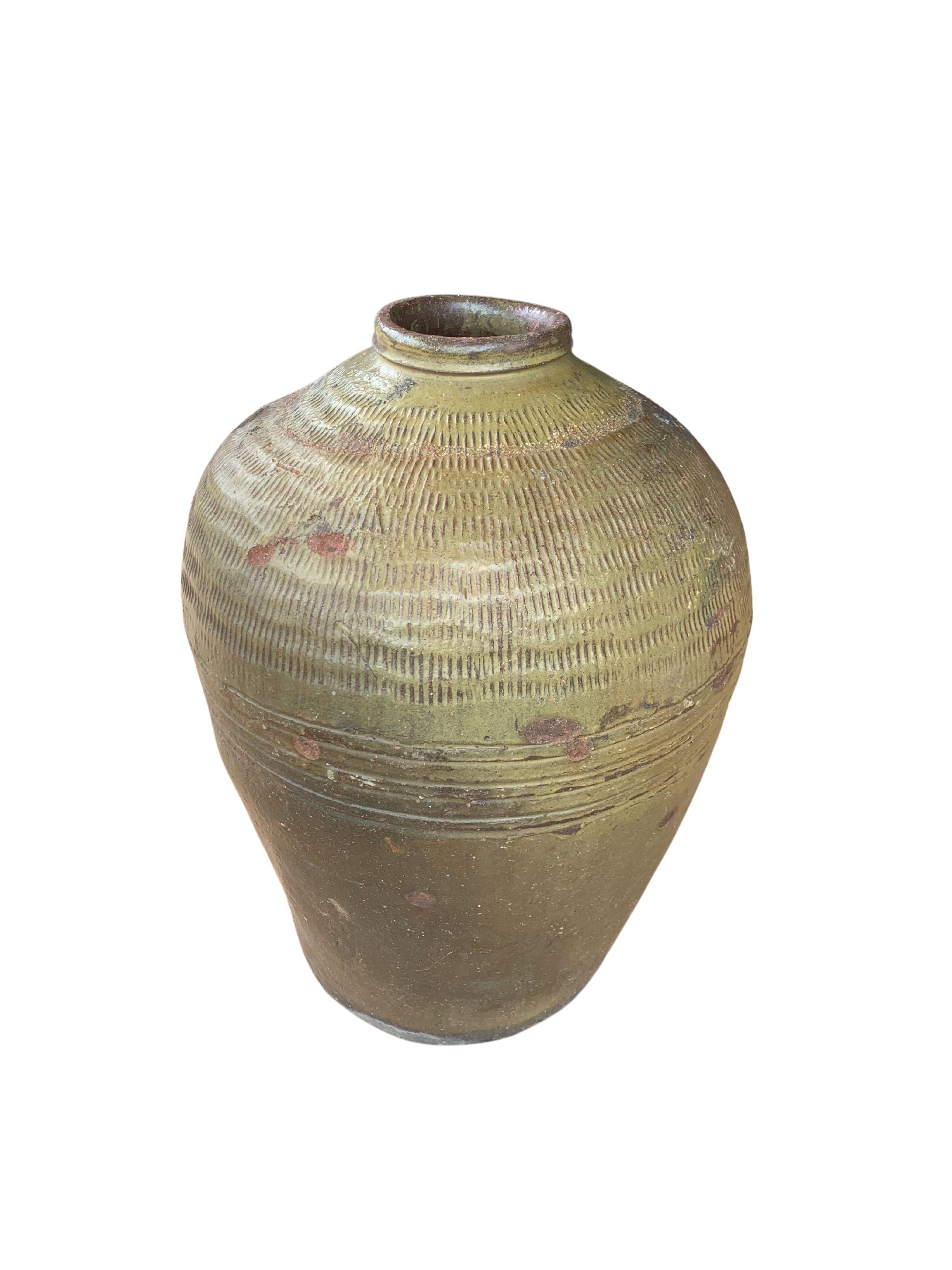 This glazed Chinese ceramic jar from the turn of the 19th Century was once used for pickling foods. It features a jade green finish and outer surface that features a ribbed texture. A great example of Chinese pottery, with its imperfections and