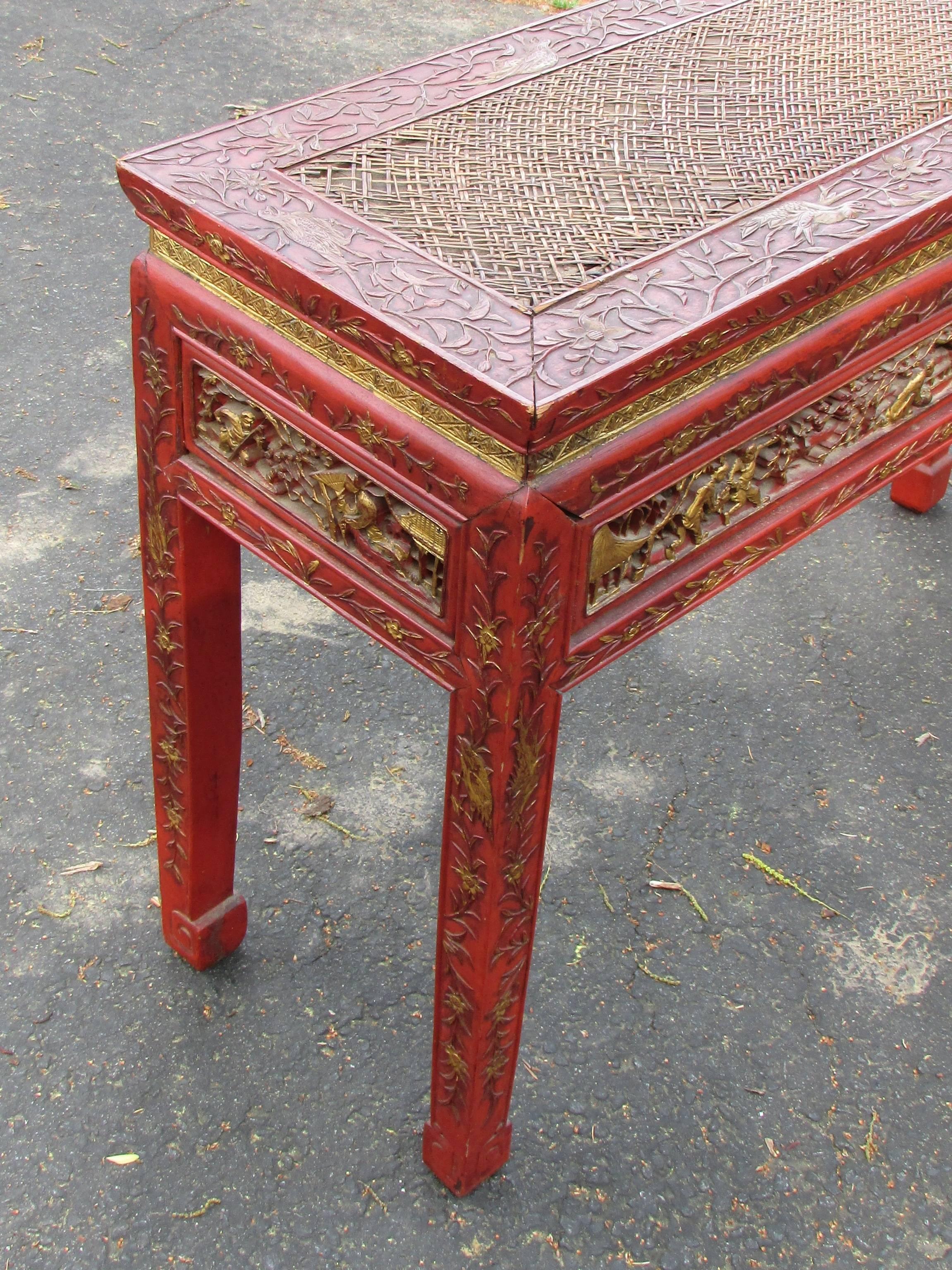 Red lacquer and gold hand carved chinoiserie console table with rattan top. This table is in original condition showing age and loss to one panel and to rattan top.