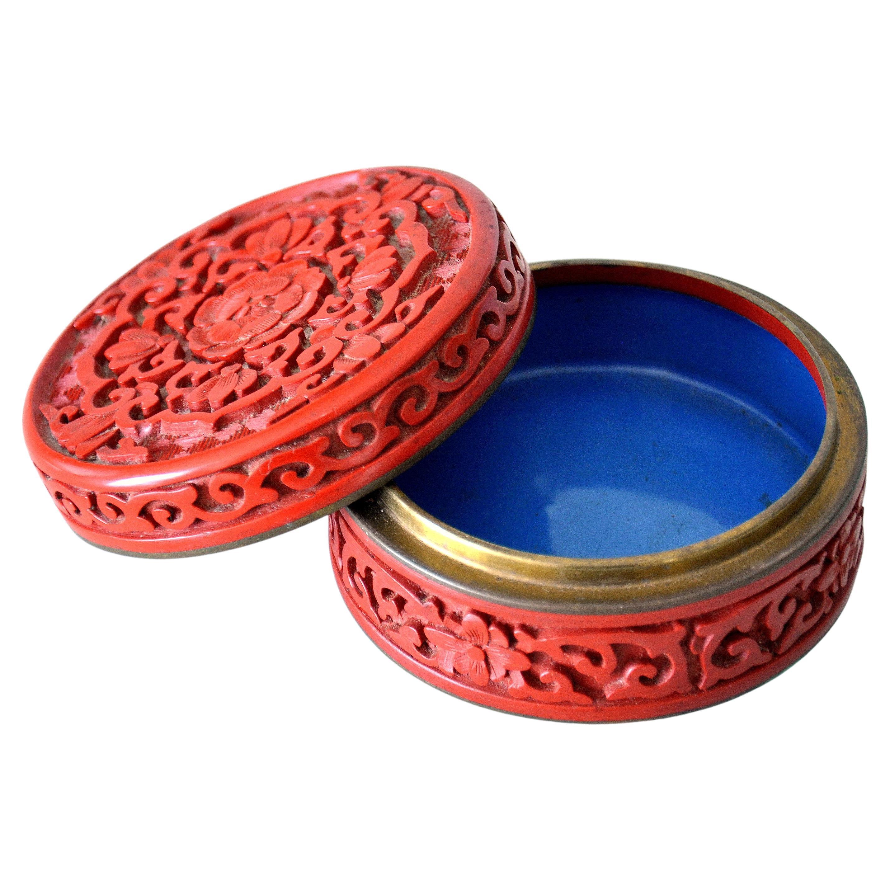 A crisply carved antique Chinese red cinnabar lacquer lidded round box with blue enamel interior and brass fittings. The 