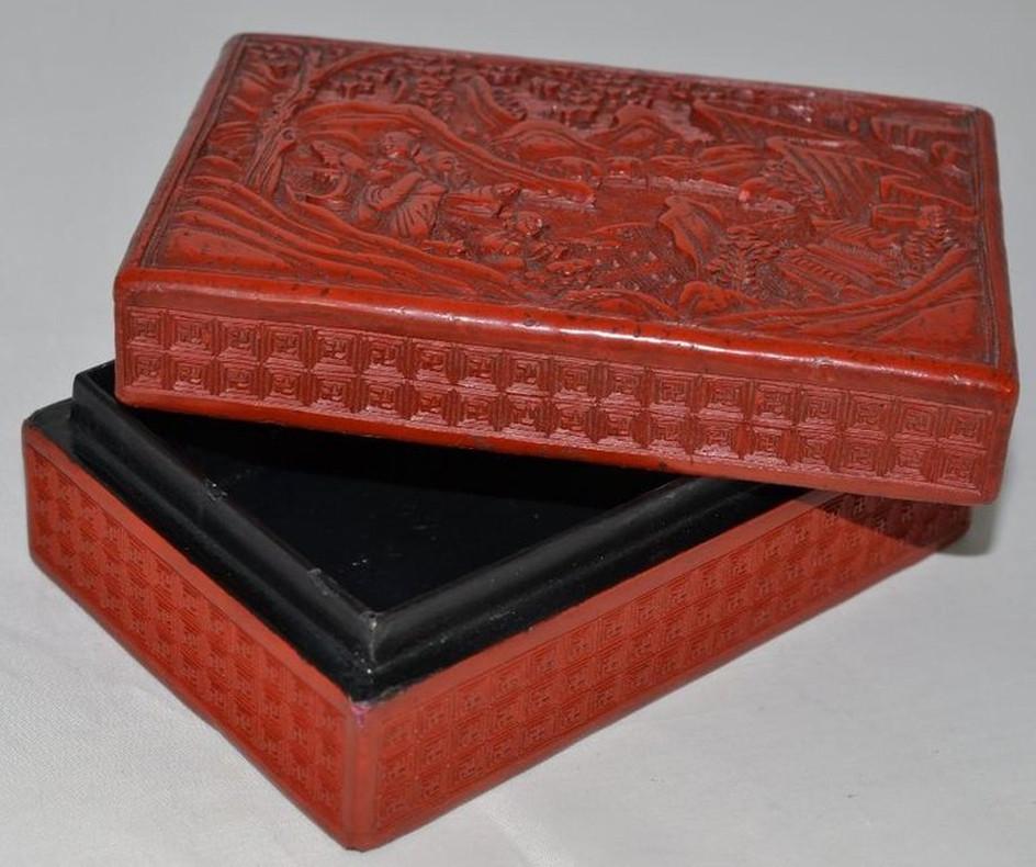 Red lacquer box with the lid to depict a scholar and children at play within a mountainous garden setting, the exterior sides covered in repeating geometric patterns. 14.5 cm wide.