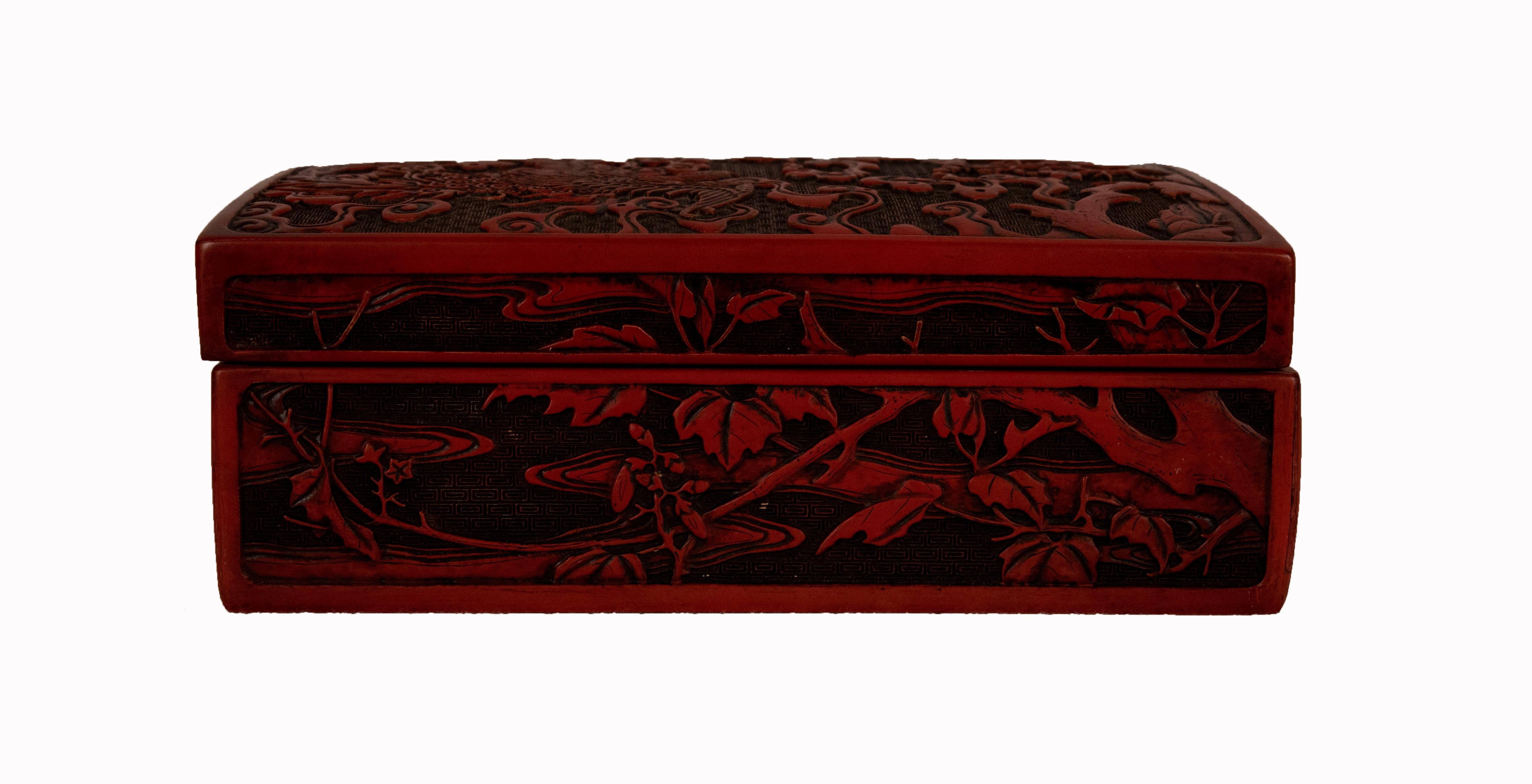 Chinese rectangular hand carved cinnabar box. The lid depicts a flying phoenix or Fenghuang surrounded by clouds above a landscape. The box was made in China circa 1900 and has a red exterior and a black lacquered interior.