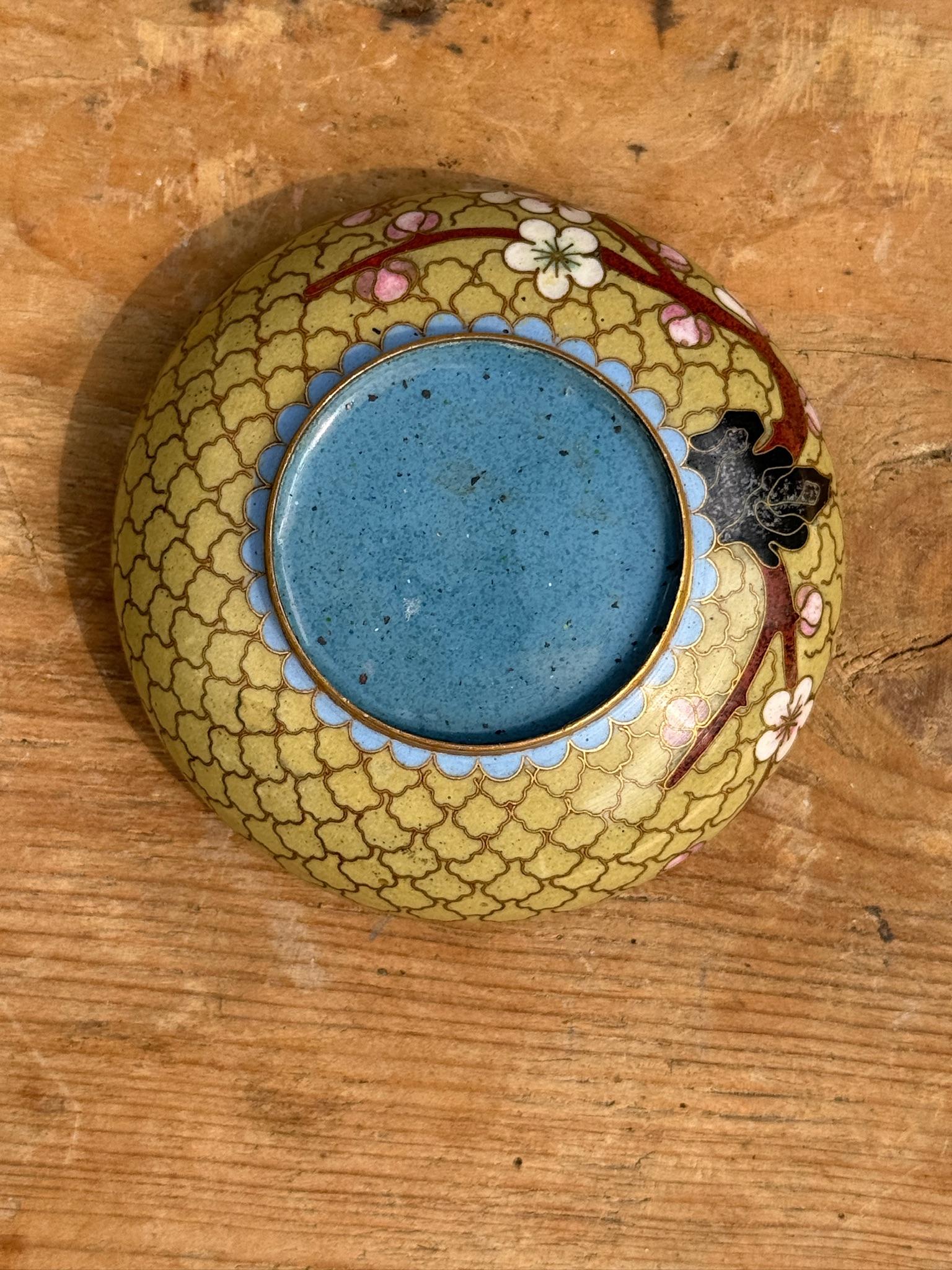 Añade un toque de elegancia atemporal a tu colección con este impresionante cenicero chino antiguo de cloisonné. Con un trabajo de esmalte sobre una base de latón, este cenicero muestra un dibujo geométrico de nubes en suaves amarillos y azules,