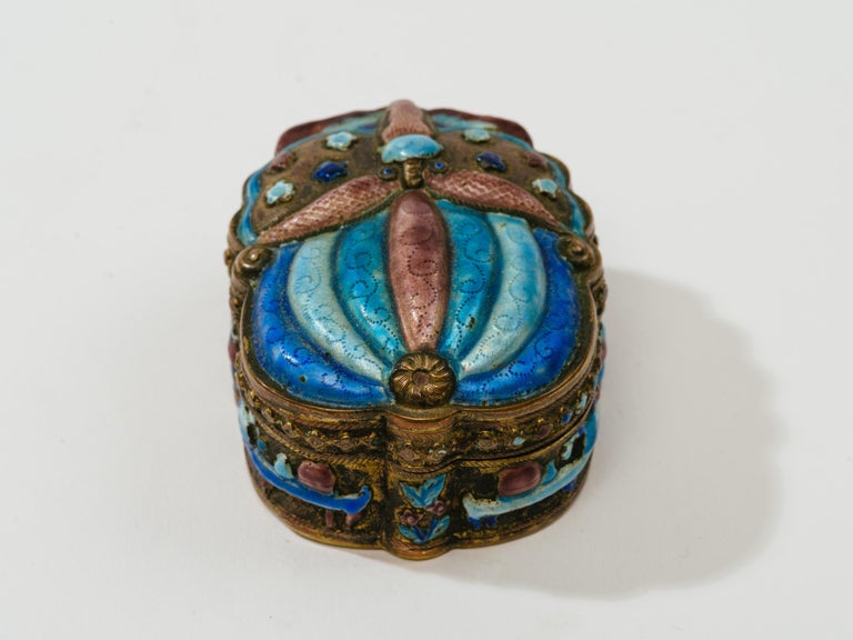 Finely detailed champlevé scarab shape box with gilt wash interior. Traces of antique mirror on inner top. Rich colors of blue, turquoise purple finely enameled all around box.