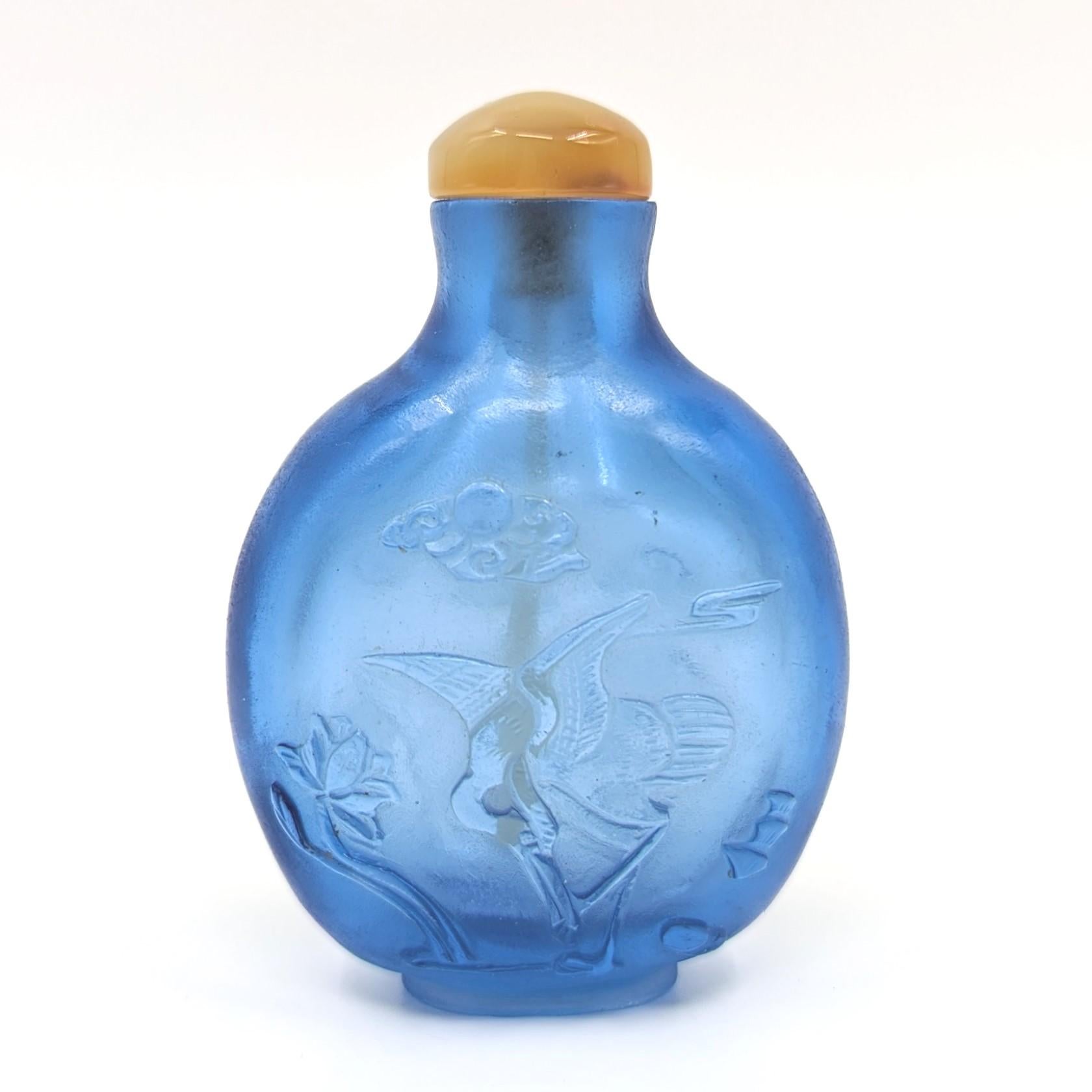 Antique Chinese light aqua cobalt blue glass snuff bottle, finely carved in relief with cranes in flight among clouds to one side, and a resting crane among lotus blooms to verso, raised on a well carved foot ring, agate stopper

19th Century, Late