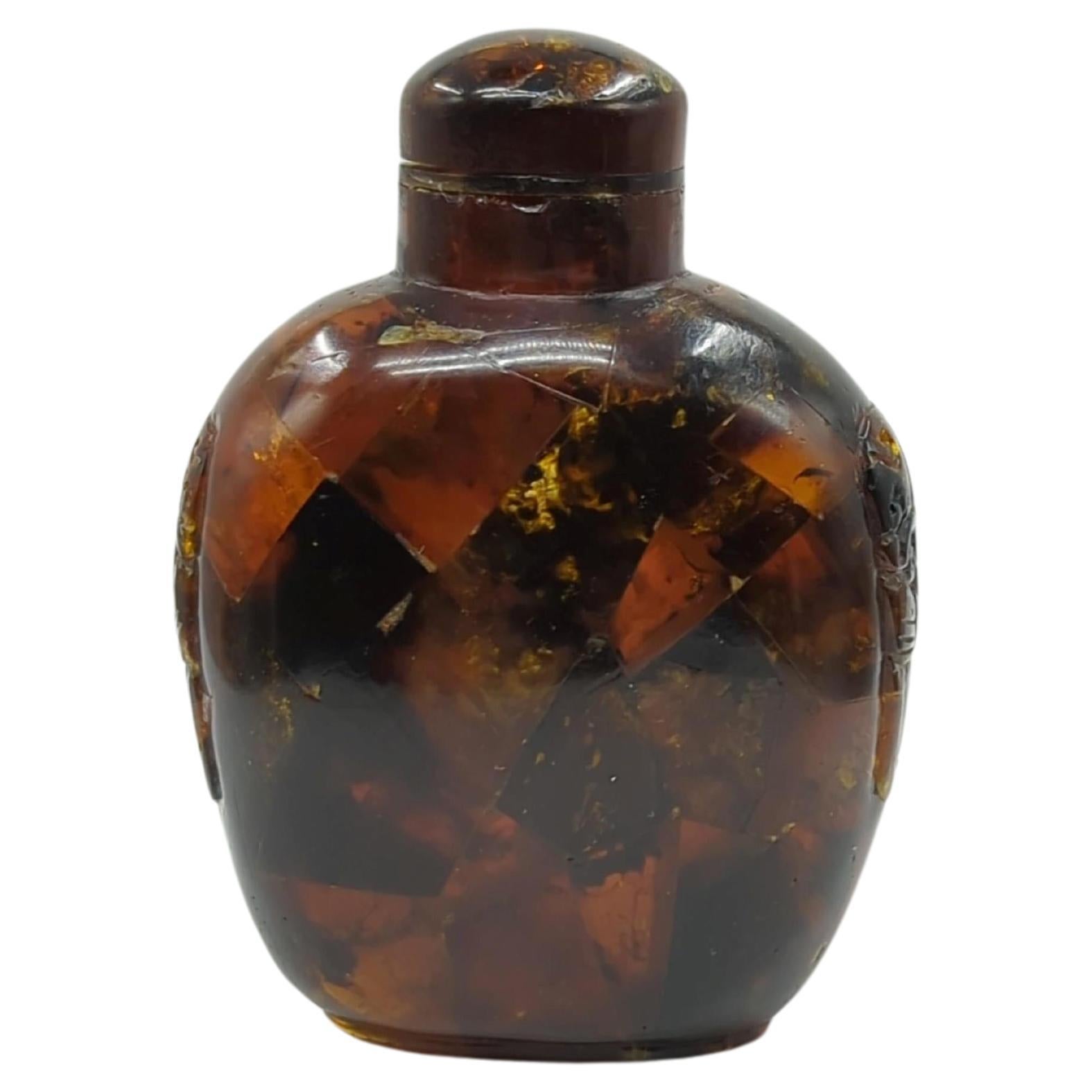 A late Qing period Chinese snuff bottle, crafted from composite amber. This bottle is adorned with meticulously carved beast and ring taotie motifs on its shoulders, and slightly raised on a carved footring. 

The use of composite amber not only