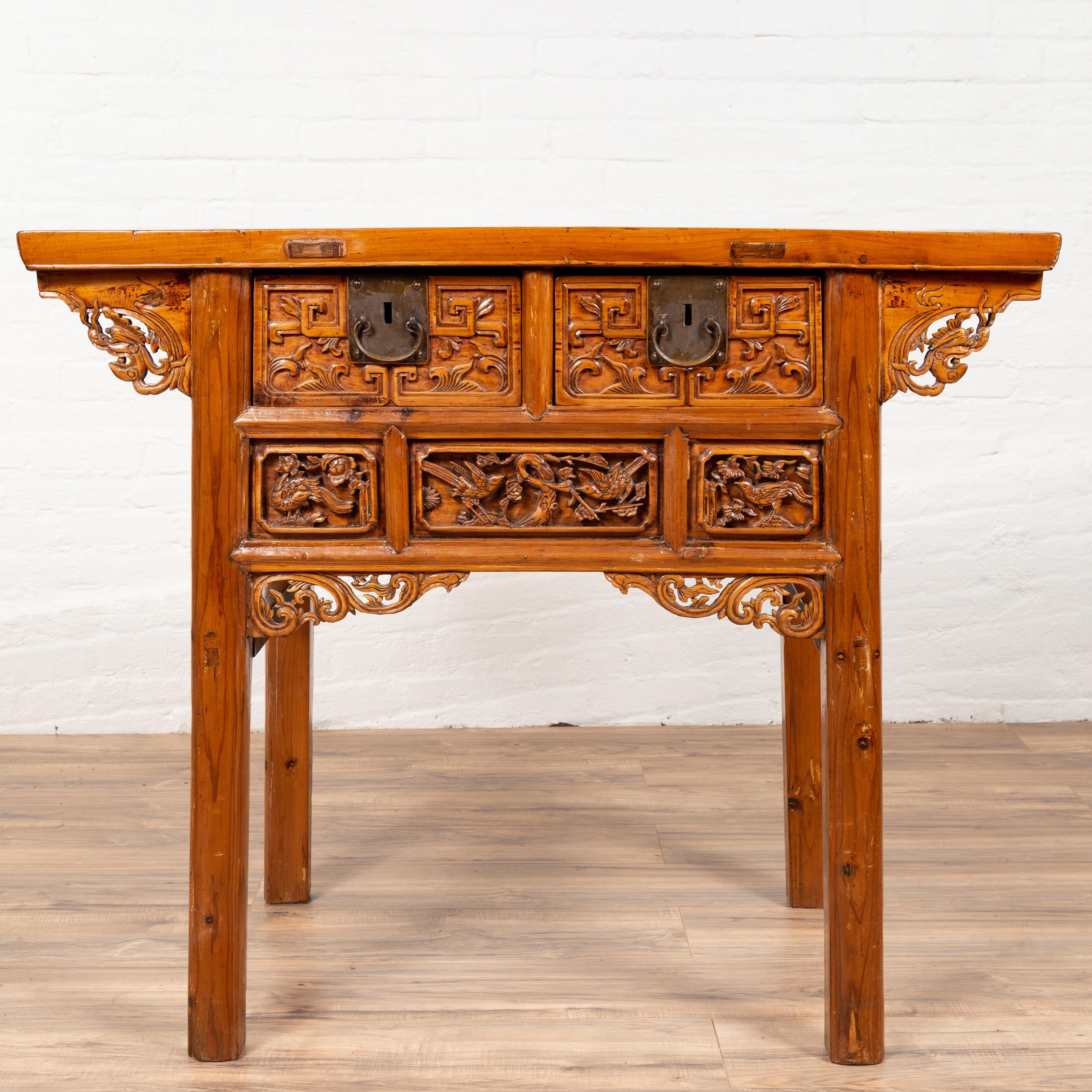 An antique Chinese display cabinet console table from the 19th century, with overhang top, hand carved décor and bronze hardware. This Chinese console table features a rectangular planked top, overhanging an exquisite façade, made of two drawers,