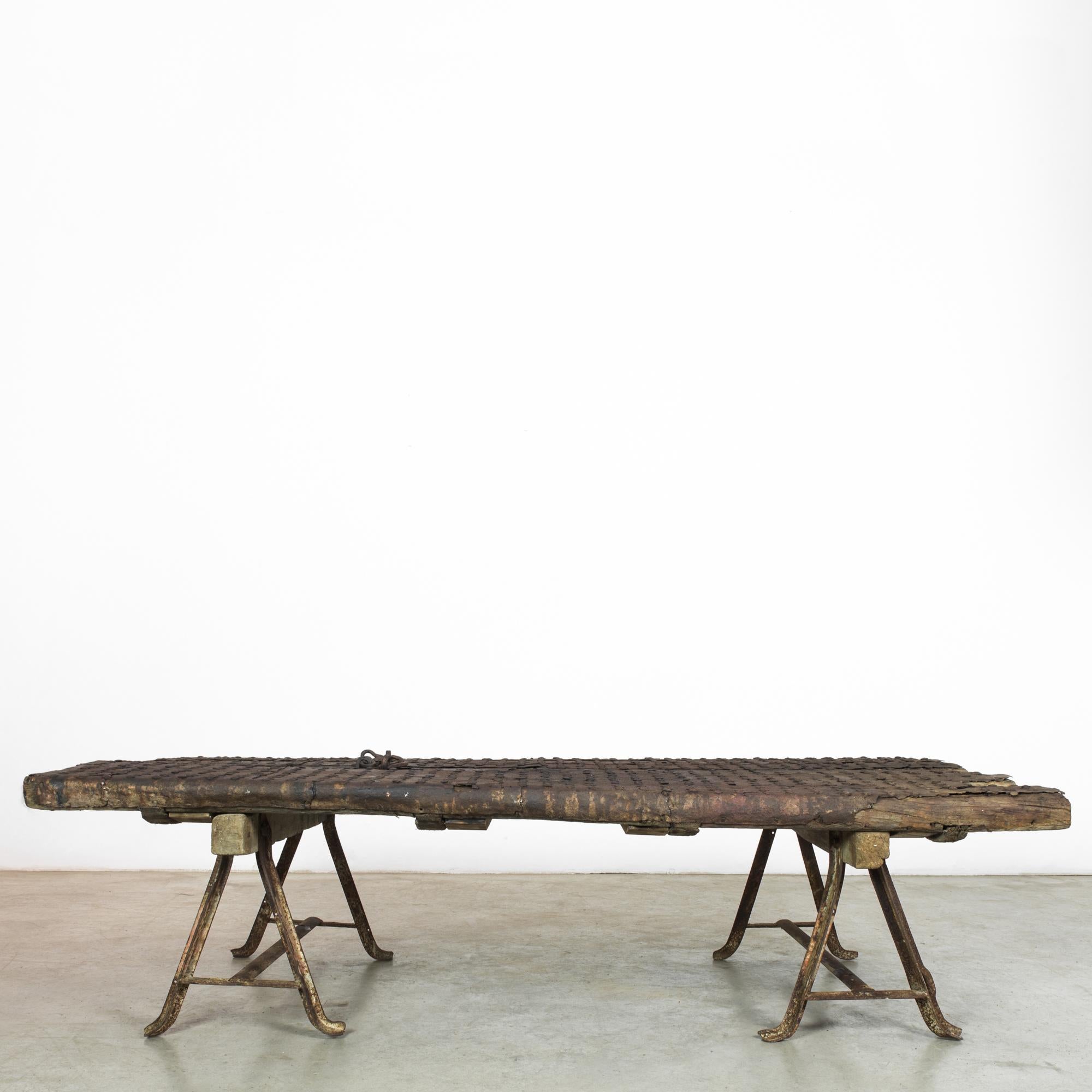 A wooden and metal door from China, circa 1900, rests on two sawhorses. The astounding patina reveals the traces of time. Metal spheres dot the entire surface, giving the doors a textured, handcrafted quality. Welded steel A-frames grip hefty wooden