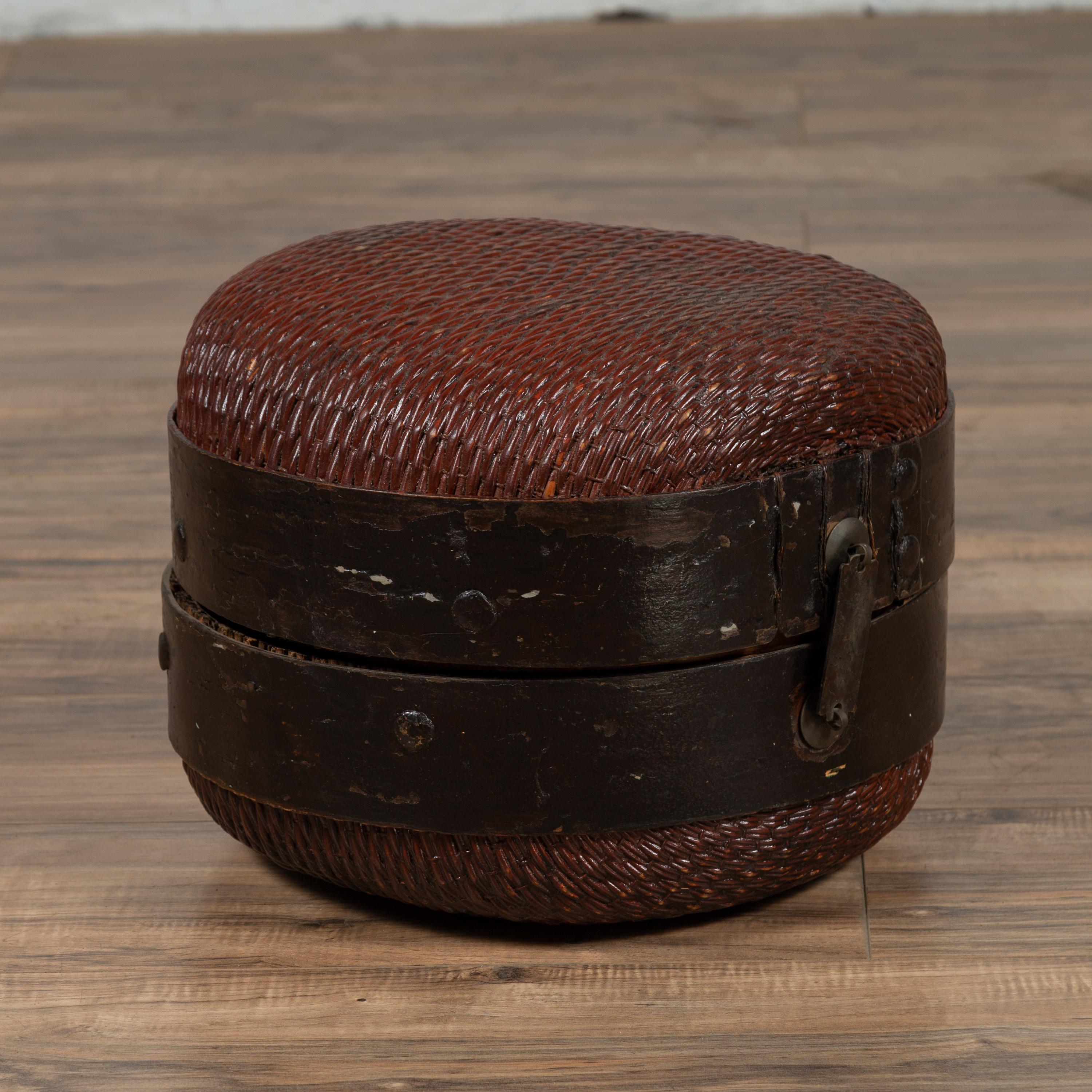 An antique Chinese rattan hat box from the early 20th century with weathered patina. We have similar ones available. Born in China during the early years of the 20th century, this rustic hat box features a rattan body, secured in the middle by dark