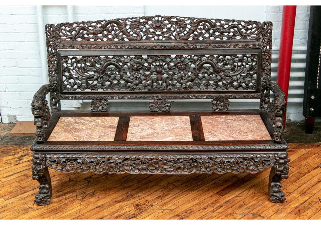 A very fine antique bench with masterful carving, superb proportions and in all original condition. The crest rail and back with openwork panels of confronting dragons in the clouds. Dragon form heavy carved arms. The seat with three pink marble