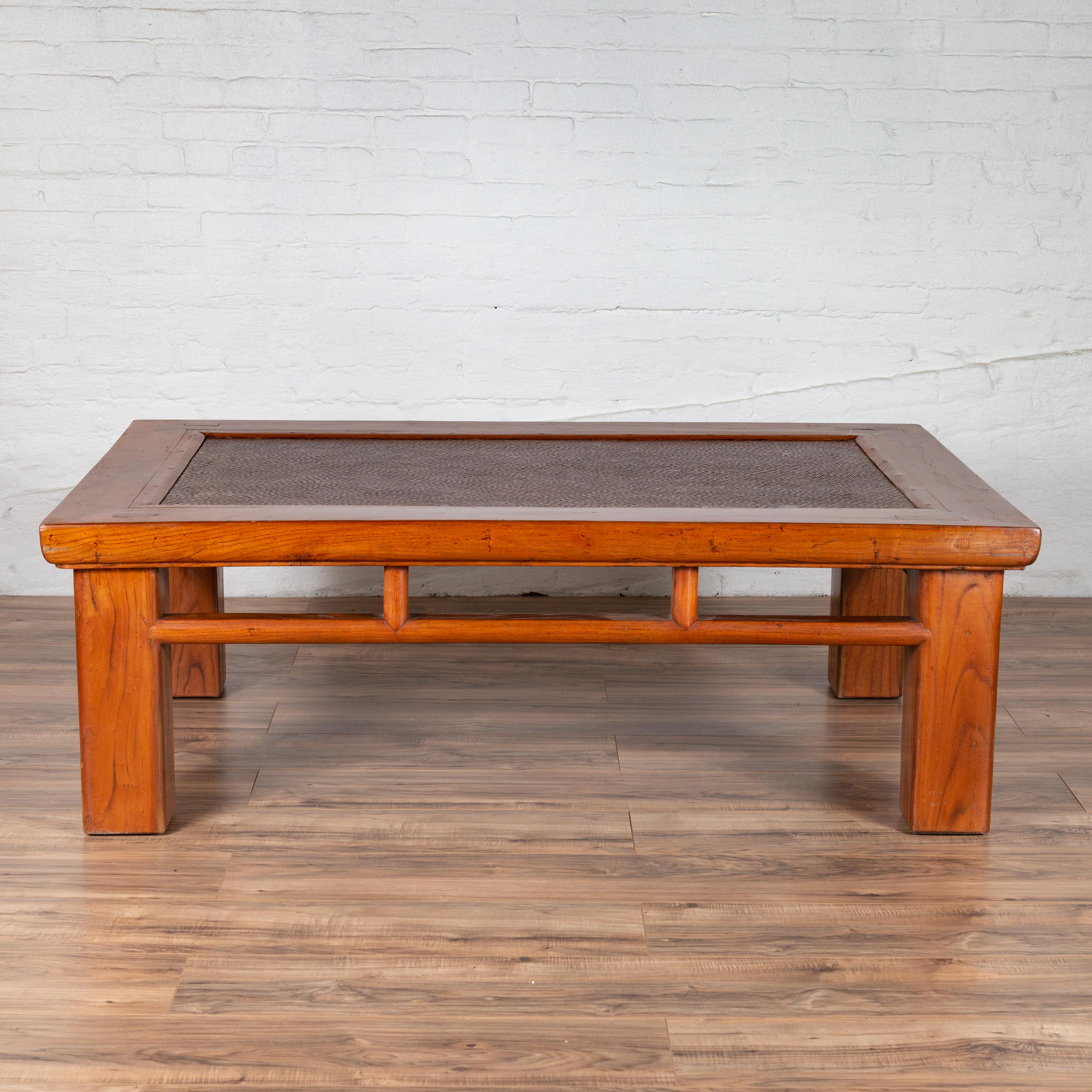 An antique Chinese elm coffee table from the early 20th century, with square legs, pillar-shaped strut motifs and rattan inset. Born in China during the early years of the 20th century, this Chinese coffee table features a rectangular top with