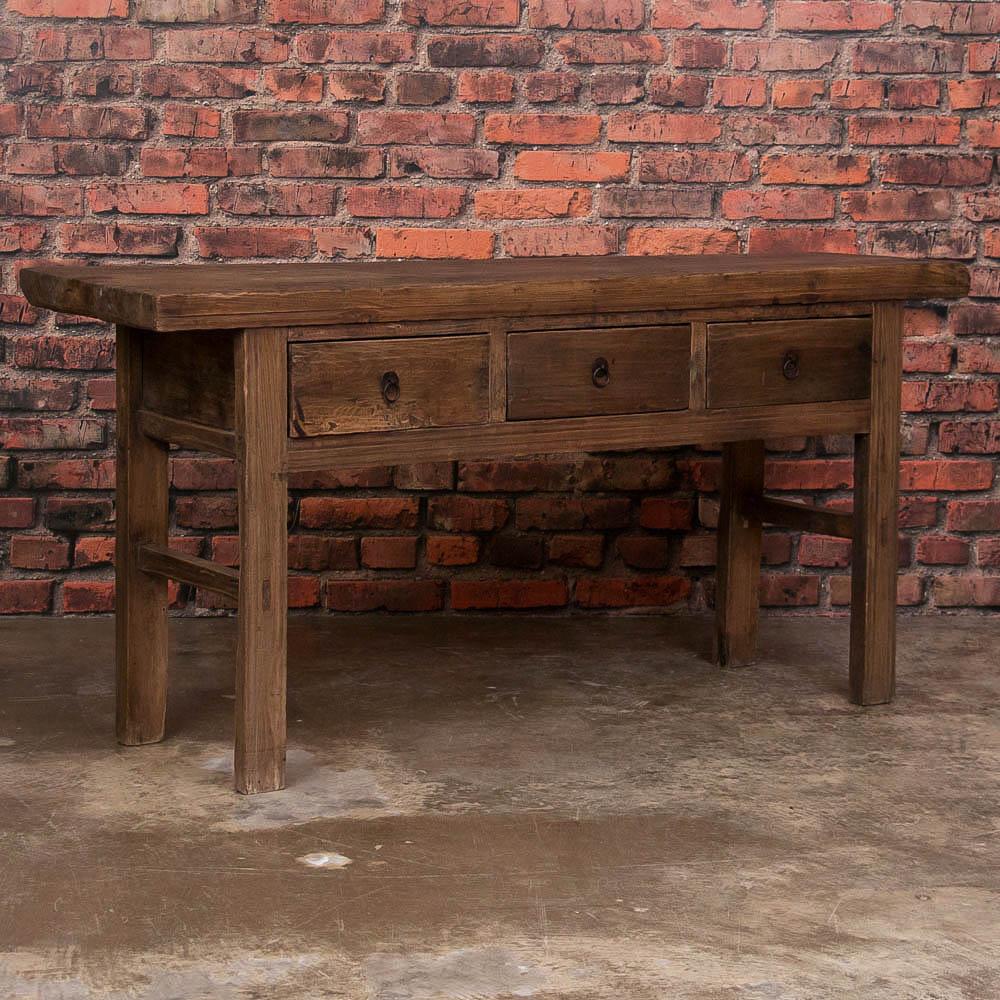 This mid-19th century elm console table's simple and clean lines give it a country feel and would make a great server or buffet. It features three drawers with metal ring pulls and is supported by elongated legs. The natural wood has a very 