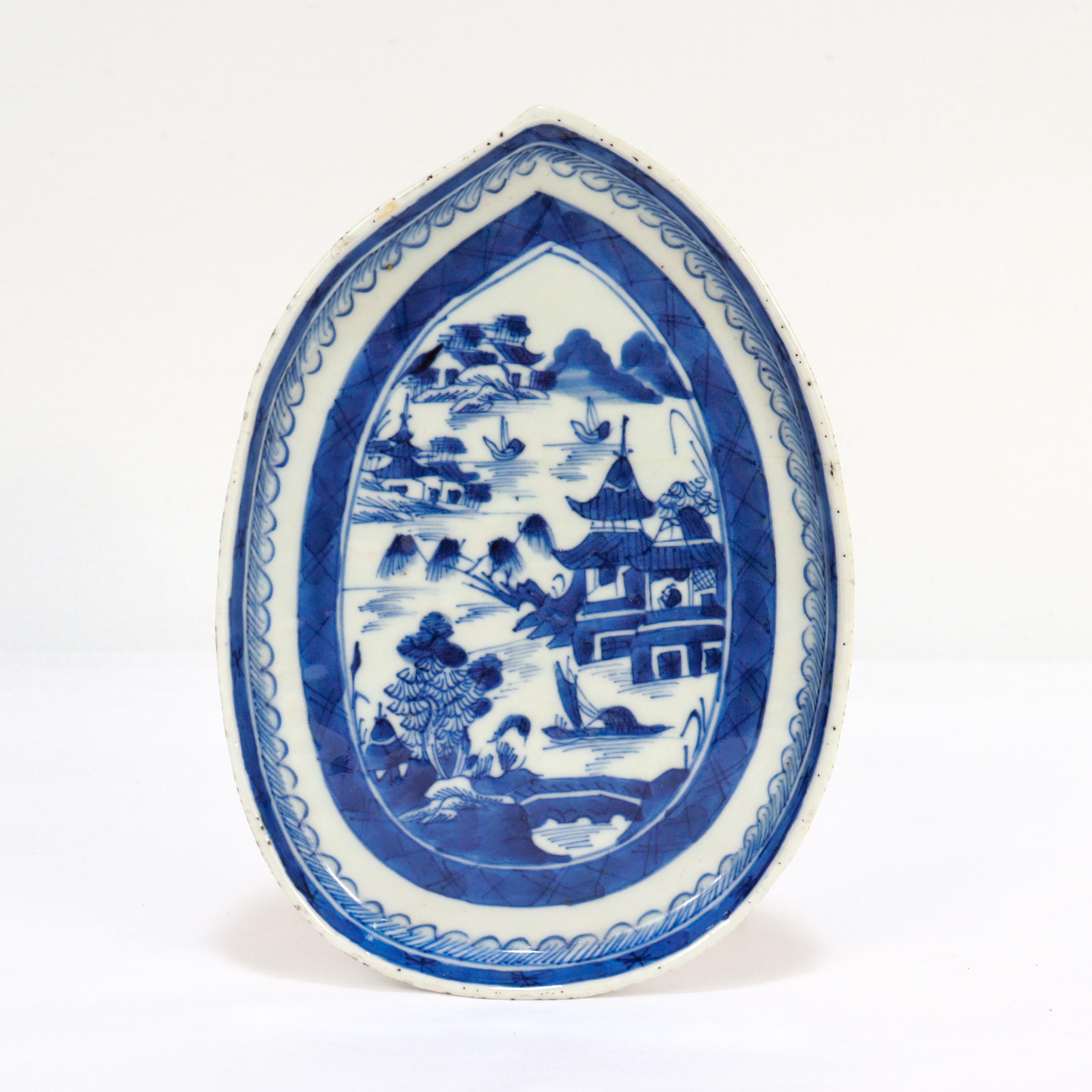 A fine antique Chinese Export porcelain bowl or vide poche.

In the Canton pattern.

In a leaf-shaped form.

Decorated in underglaze blue with a mountainous Chinese village with houses, mountains, foliage, and a river and boat. 

Having an unglazed