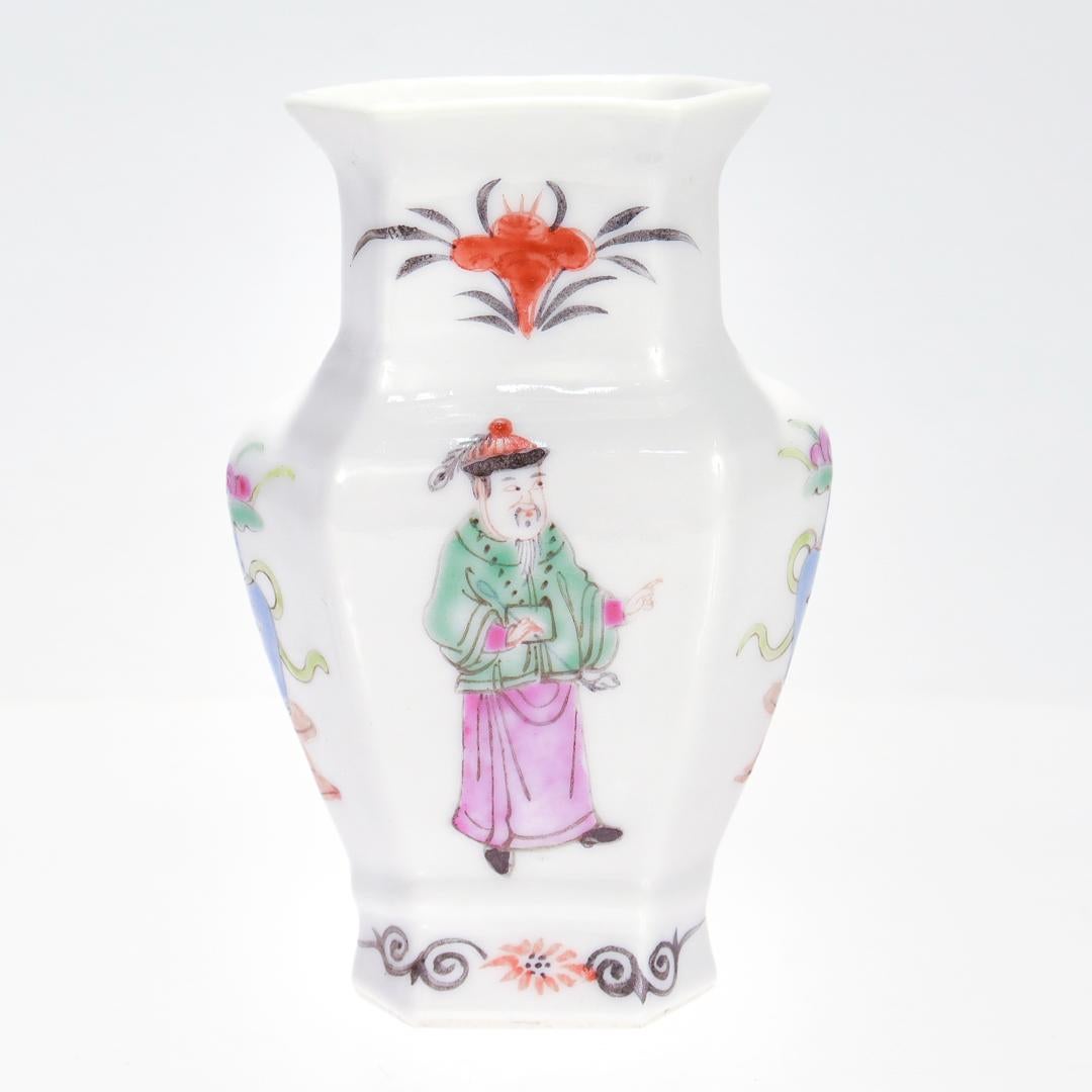 Un pregiato vaso da bocciolo in porcellana cinese da esportazione o un vaso da armadio in miniatura.

Con un fondo di porcellana bianca e un corpo sfaccettato a sei lati.

Sui lati lunghi sono dipinti rispettivamente un anziano e un giovane in abiti