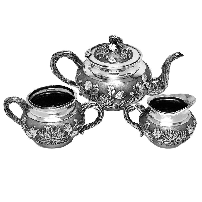 A lovely Antique Chinese silver tea set comprising of a Teapot, Sugar Bowl and Milk / Cream Jug. Each piece is embellished with beautiful chased designs featuring chrysanthemums and the handles, spout and finial are fashioned to look like stylised