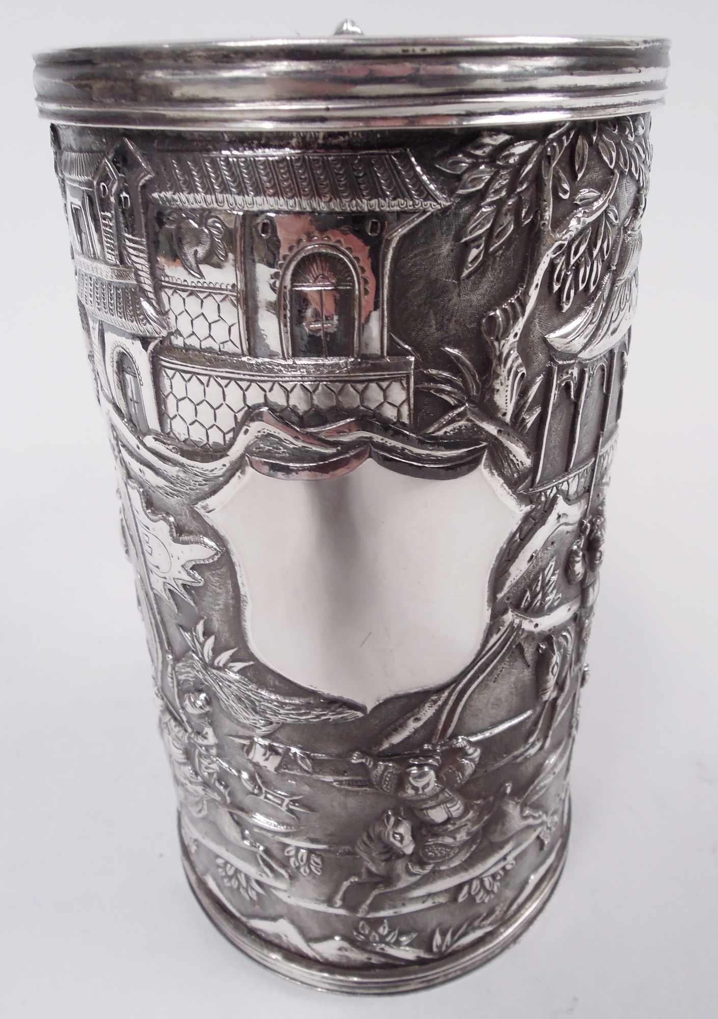 Chinese export silver mug, ca 1880. Straight and upward tapering sides with allover low-relief battle frieze depicting soldiers—spearmen, lancers, and swordsmen—with a few hapless members of the flag corps wandering into the thick of things. In