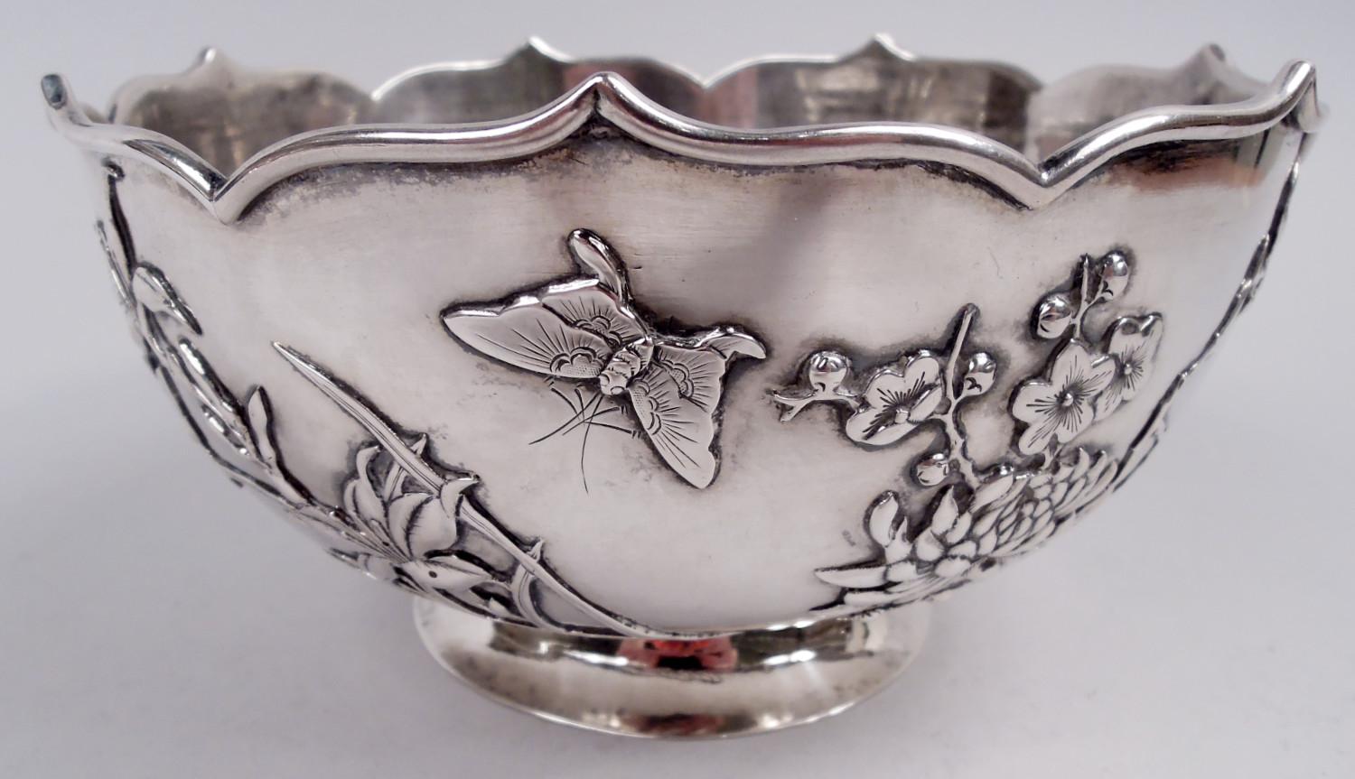 Ciotola d'argento cinese da esportazione, 1910 circa. Curva e affusolata con bordo modellato a ogiva; piede rialzato e divaricato. Ramo di prunus in fiore, magnolie e gigli con farfalle che sfrecciano sopra la testa. Telaio a coste e a lobi
