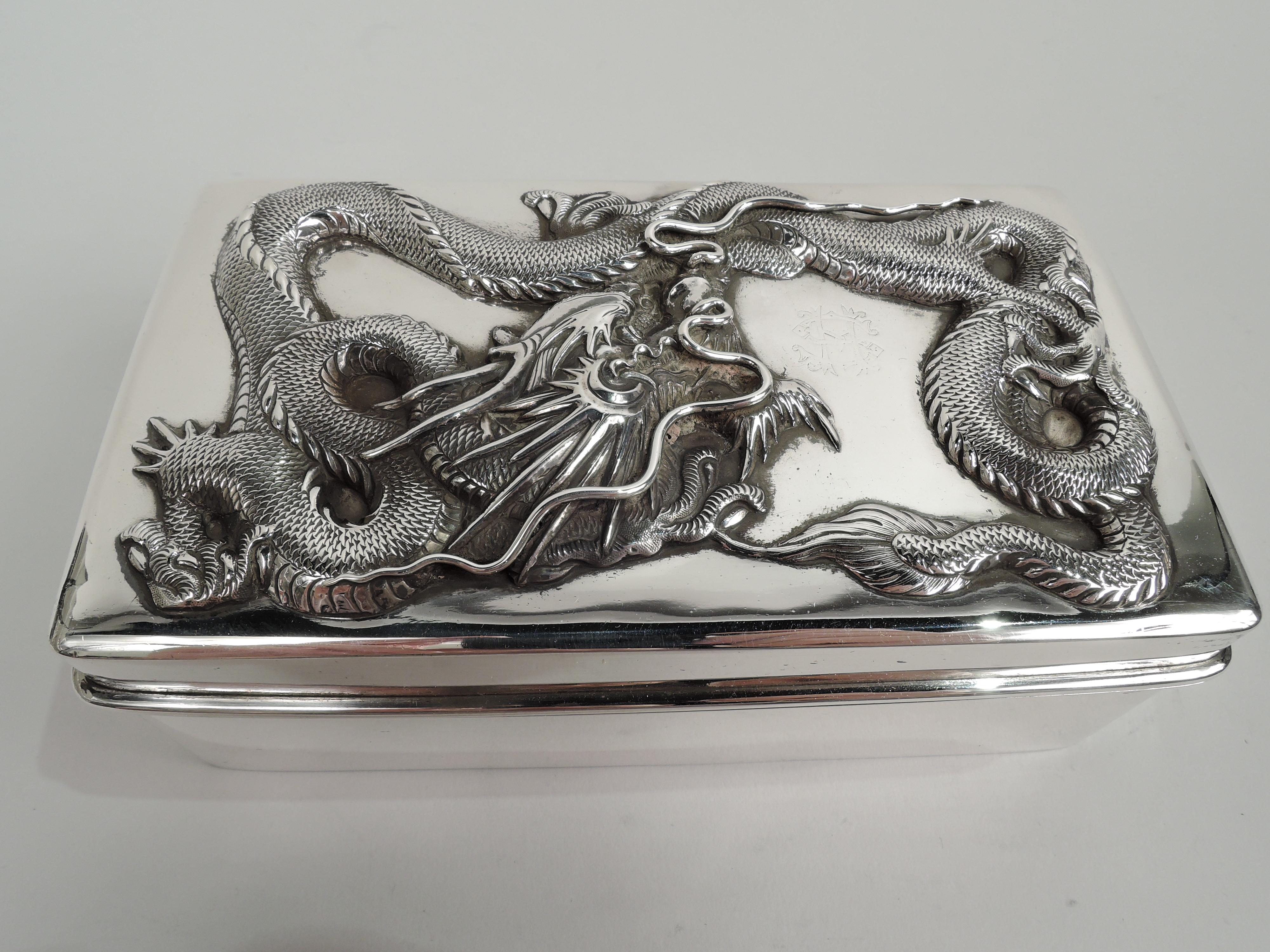 Turn-of-the-century Chinese export silver box. Rectangular with straight sides and curved corners. Cover hinged and raised with wraparound overhanging rim. On cover top is applied dragon with spiked head, sharp talons, and wraparound scaly