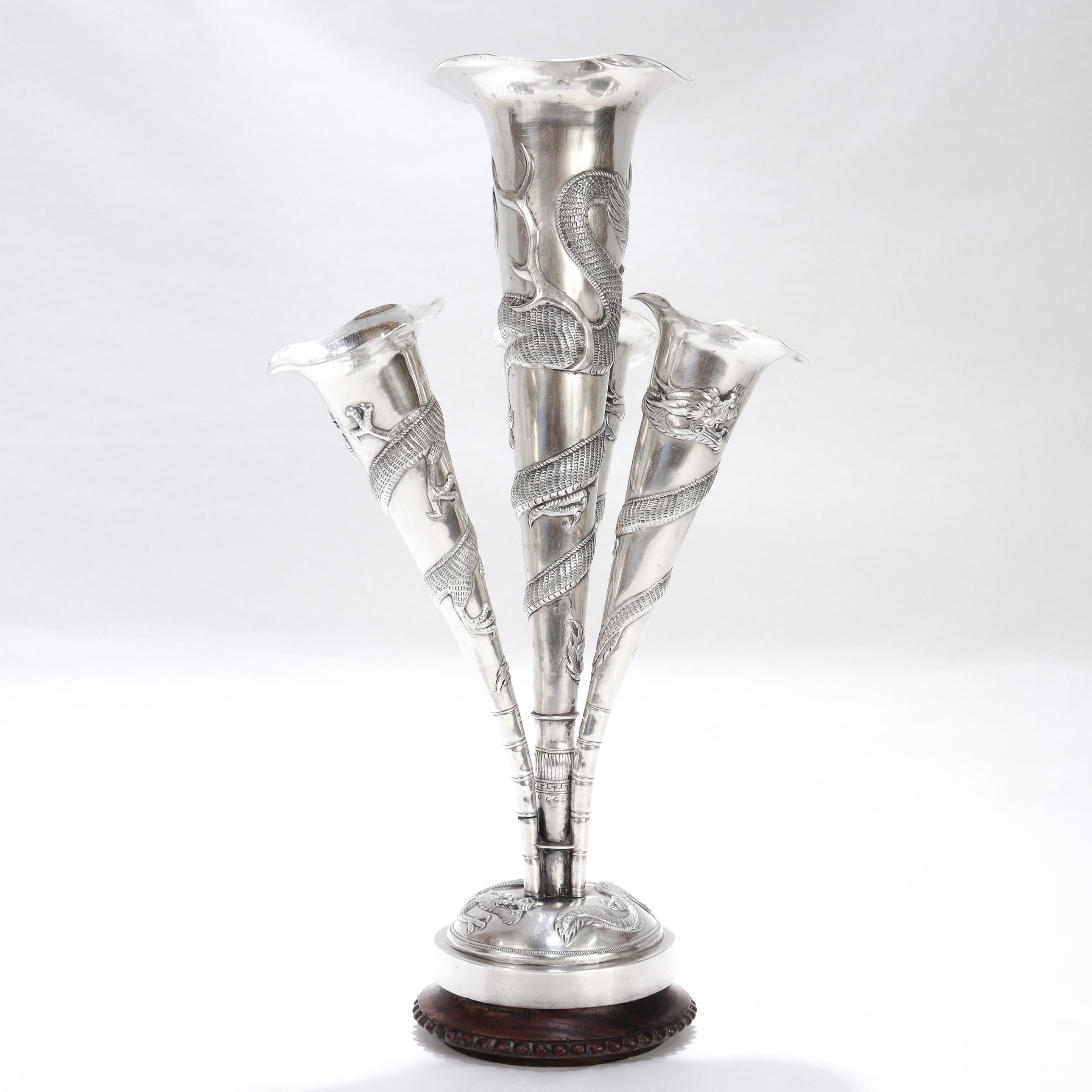 A fine antique Chinese Export silver epergne or flower vase.

By Kwan Wo of Canton and Hong Kong (active ca. 1875 - 1940).

The epergne with 4 horn shaped, tapered arms or vases, a round silver plinth, and a wooden base.

Each arm with an applied