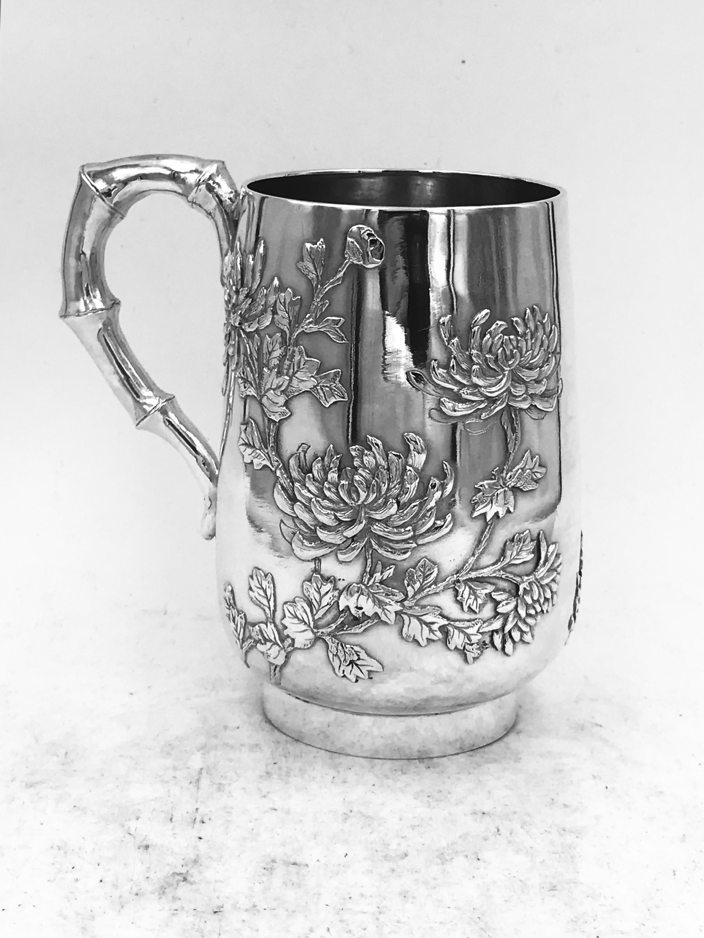 A Chinese silver mug of round form and on collet base, decorated with well detailed chrysanthemum on a plain background, and a simulated bamboo handle. Marked with 'TS', which was used by Tien Shing' (天盛, 1870s--) and 'Tai Sang' (大生, 1900s--), both