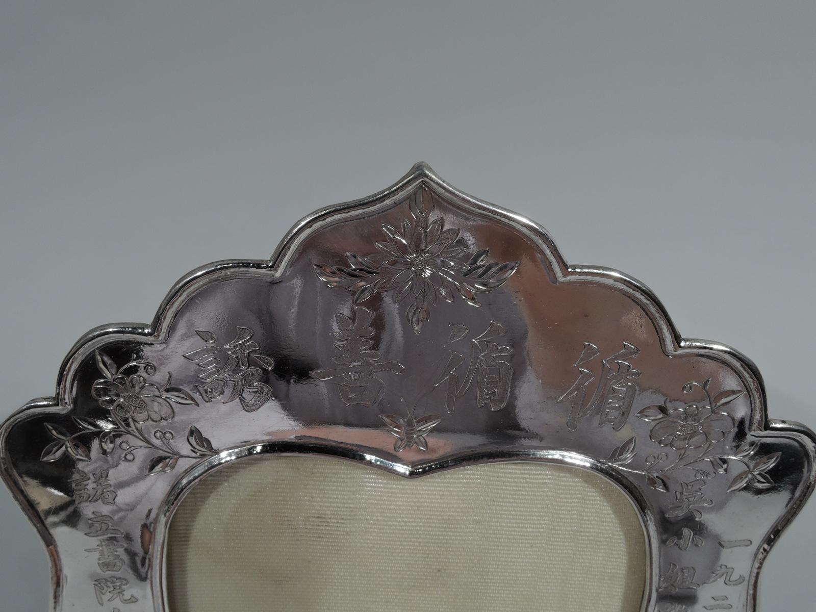 Chinese export silver frame, circa 1910. Heart-shaped window in shaped surround with scalloped ogee top and scrolled bracket feet. Engraved Chinese characters and blossoming branches. With glass, silk lining, and hinged wire support. Marked with