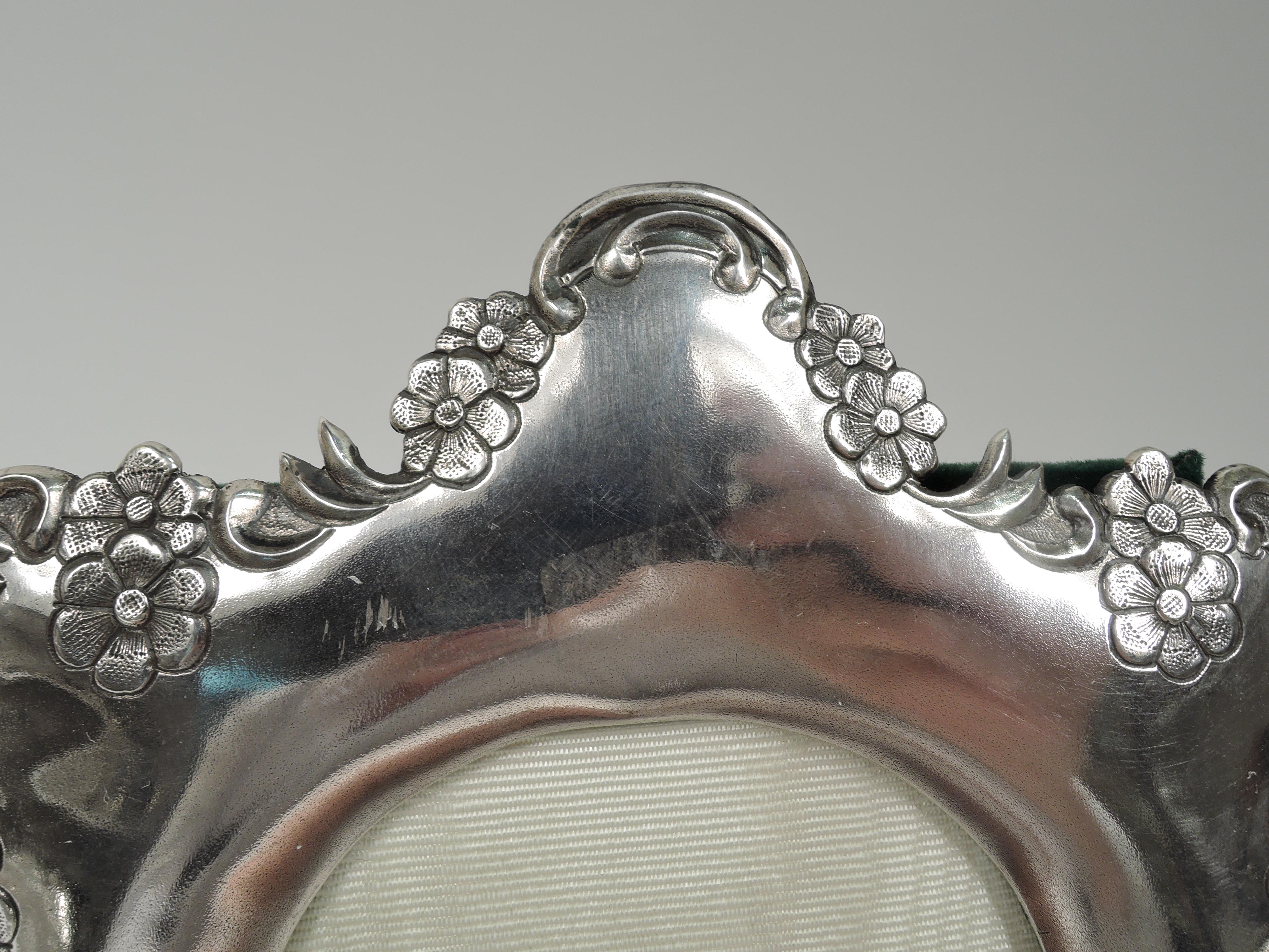 Turn-of-the-century Chinese export silver picture frame. Oval window in shaped surround with scrolls and flower heads at top, and leaves, stars, flowers, and heart cartouche vacant on stippled ground at bottom. With glass, silk lining, velvet back,