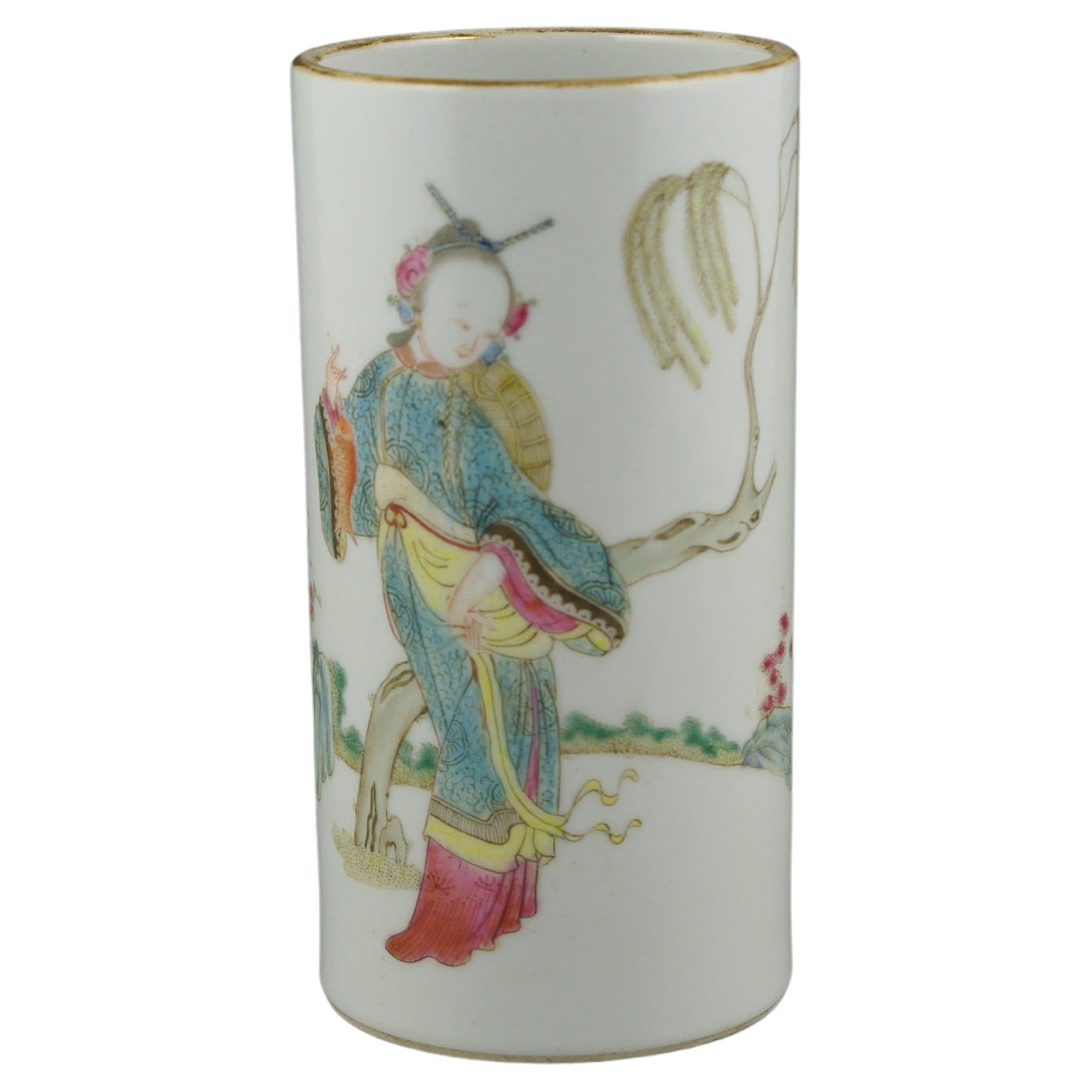 An antique Chinese porcelain brush pot, finely painted in famille rose fencai, of a court lady in a rocky garden scene, on white ground, with faded gold glaze mouth ring, and six character apocryphal reserve seal mark to base in dark red glaze