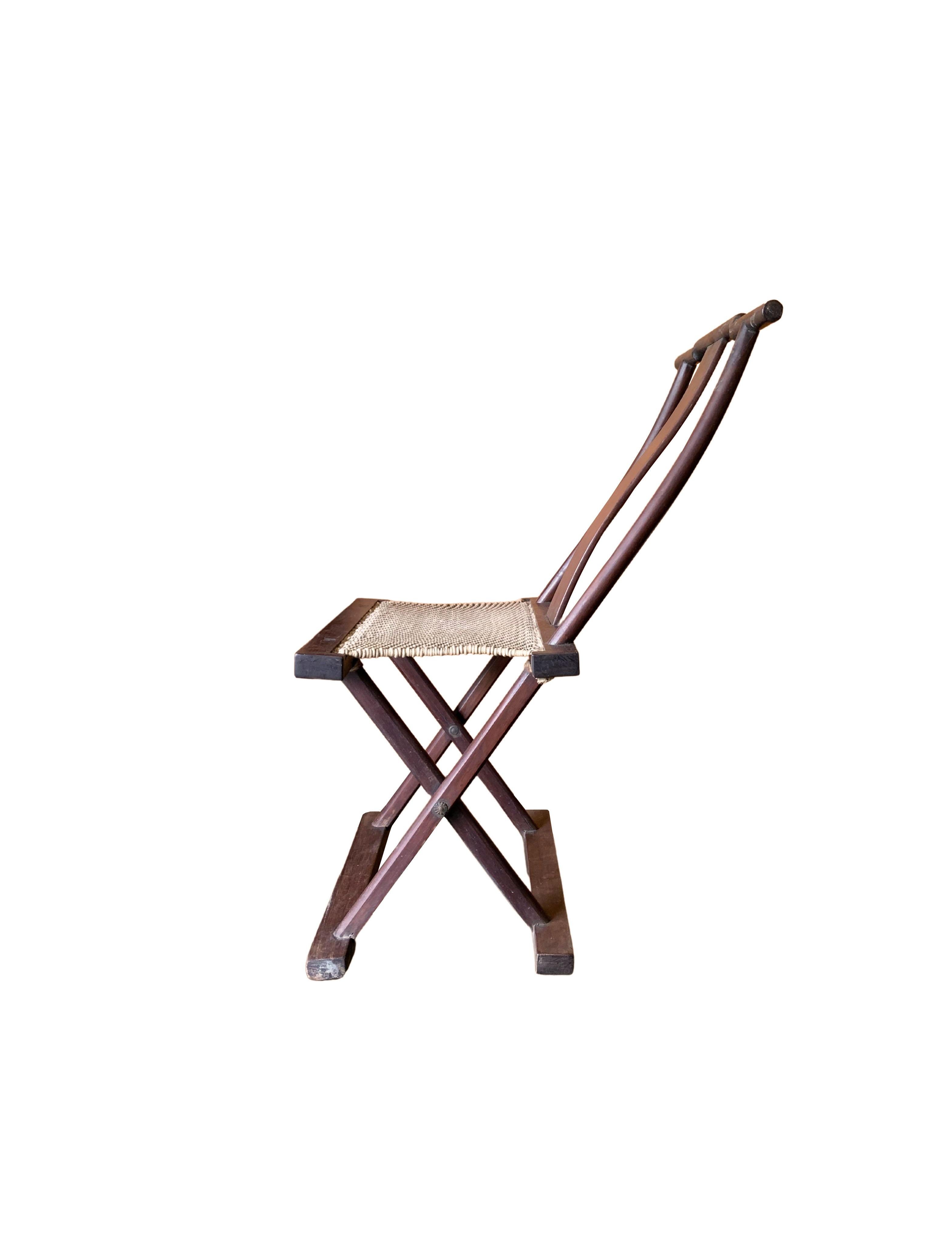Dieser aus einem Holzrahmen gefertigte Klappstuhl aus dem frühen 20. Jahrhundert wurde einst von chinesischen Reisenden benutzt. Die Sitzfläche ist aus gewebtem Stoff gefertigt, der zusammen mit der Rückenlehne für einen bequemen Stuhl sorgt. Sein