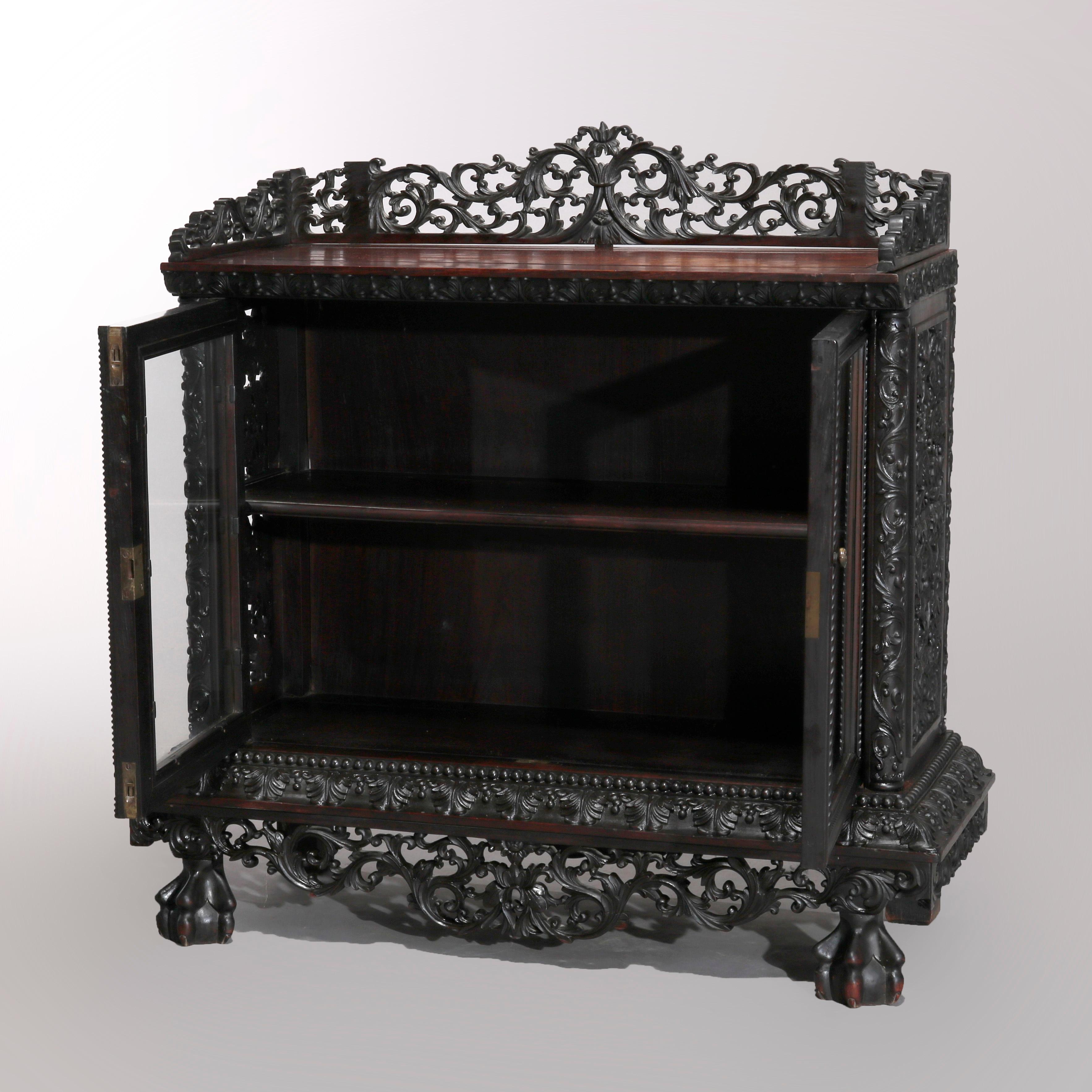 An antique Chinese double door tea cabinet offers rosewood construction with upper display having foliate carved pierced gallery surmounting case with double doors opening to shelved interior, pierced scroll and foliate skirt, raised on claw and