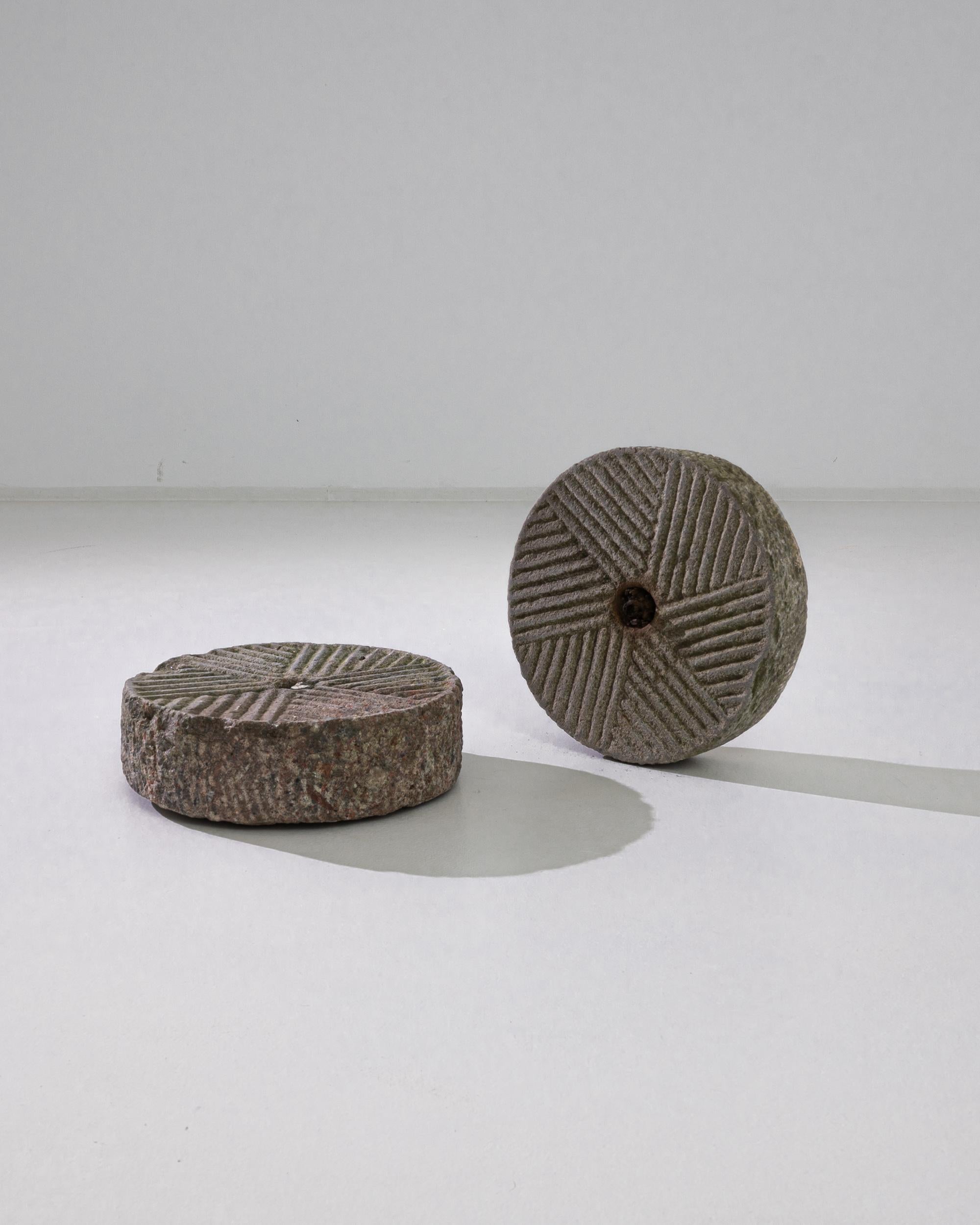 A pair of antique grindstones from China, produced circa 1900. Stone wheels with beautifully patterned criss-crossing ridges radiating out from the center, turning them into two facing suns. Traces of long gone grinds remain in the ridges as ruddy