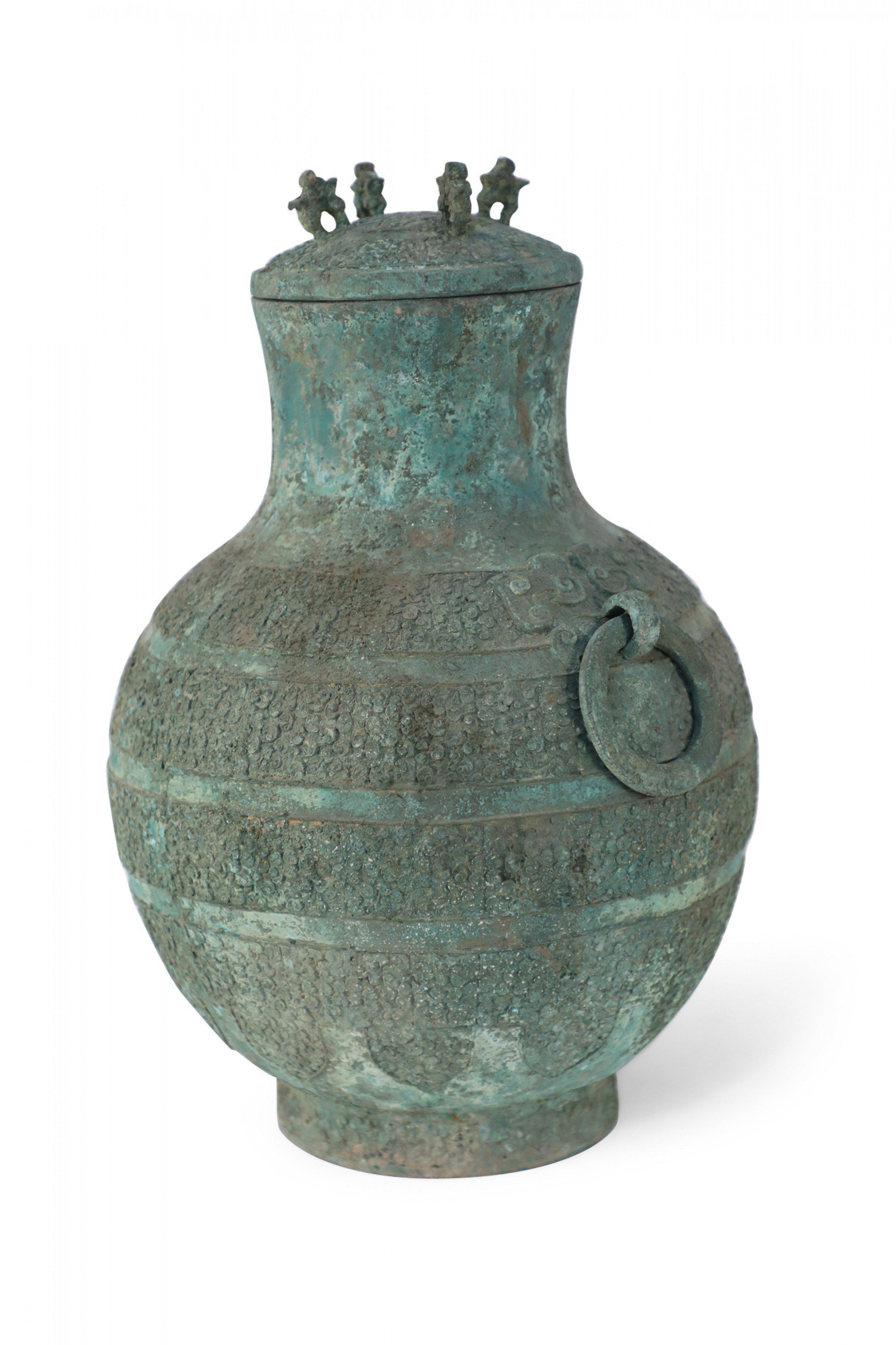 Antico vaso da vino rituale in bronzo verdeggiante di forma bulbosa in stile Dinastia Han con un motivo arcaico a bande in rilievo, un coperchio a cupola con quattro anse a forma di zoomorfo, due anelli decorativi sui lati e un piede circolare.