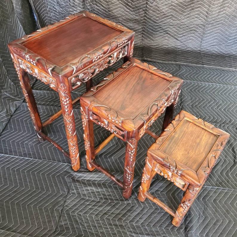 Stunning set of three exquisitely carved Chinese hardwood nesting tables from the early 20th century. Featuring intricate foliate and grape carvings, the tops with beautiful wood grain pattern, gorgeous brown/red coloring and good patina of the