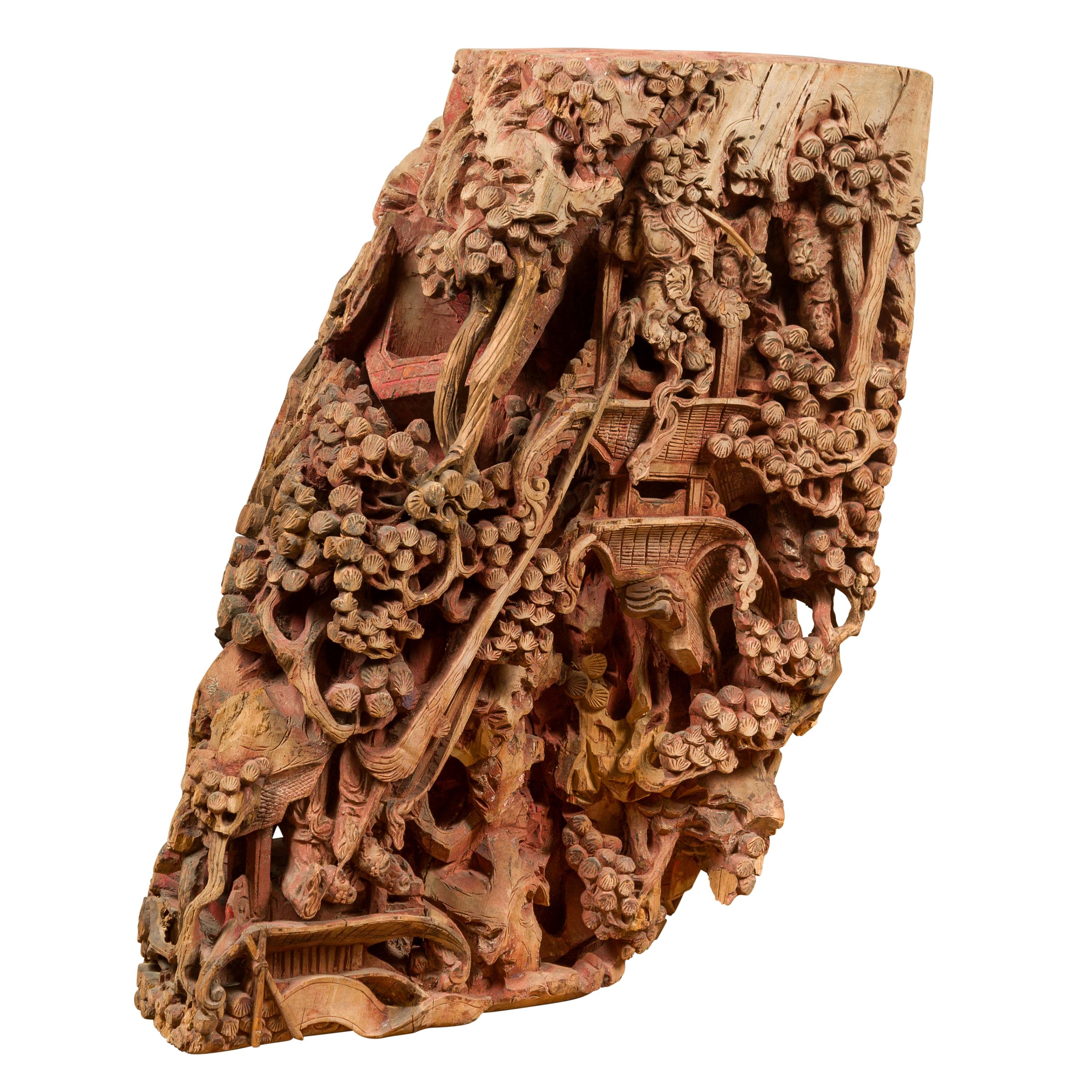An antique Chinese hand carved wooden temple corbel from the 19th century, with characters, pagodas, vegetation and red polychromy. This Chinese architectural fragment is carved with an abundant décor featuring dynamic Chinese characters actively