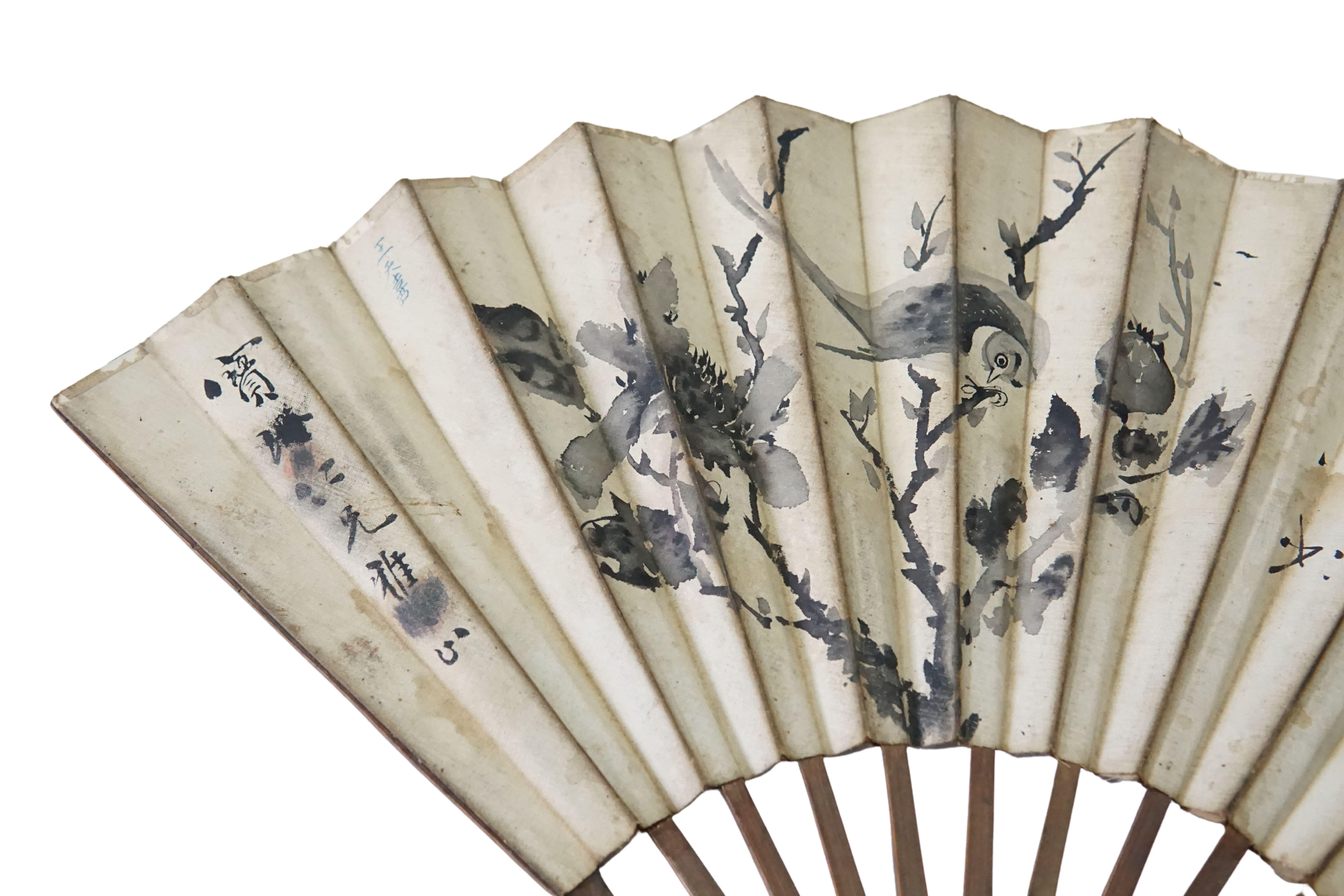 A Chinese hand-painted fan with hand-painted calligraphy (with two different drawing on either side). The fan's frame is crafted from bamboo and also includes wood engravings. The calligraphy features birds and hand-painted characters on one side &